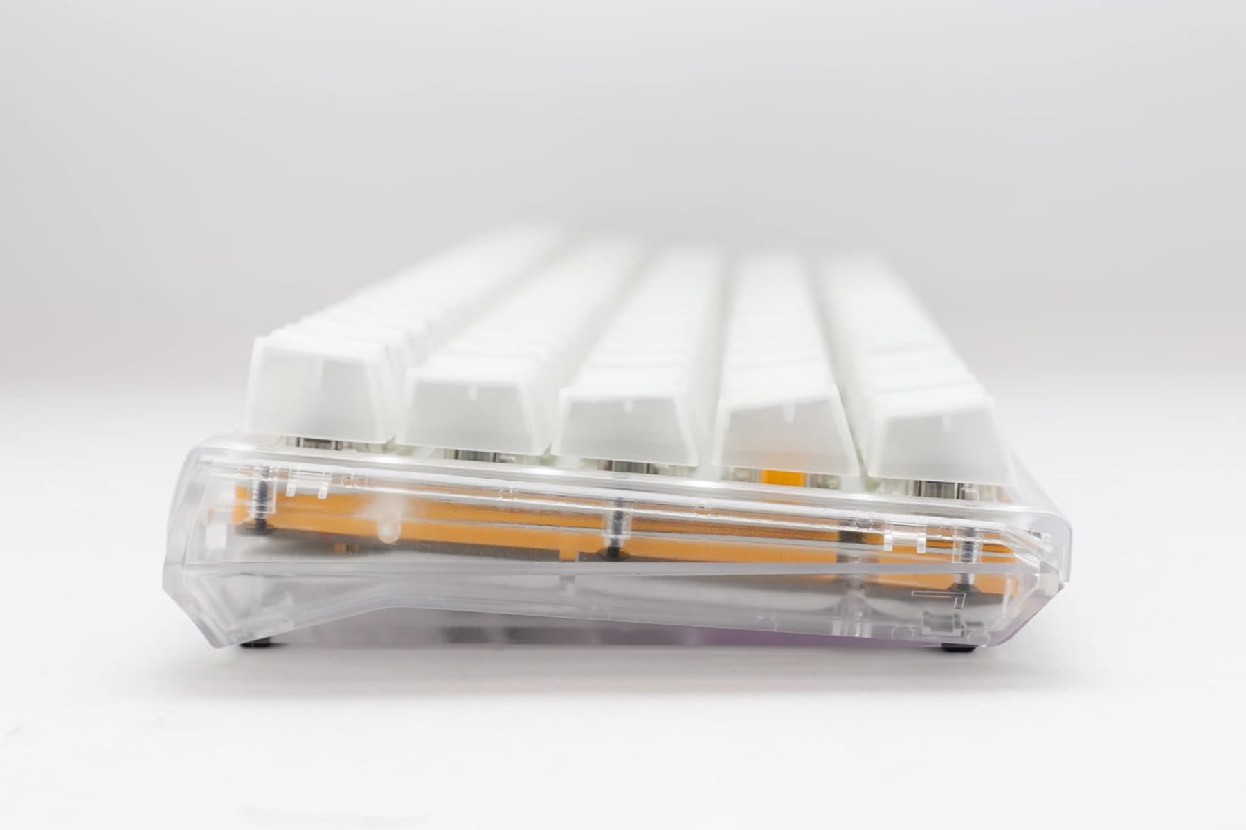 Widok z boku klawiatury z białymi nakładkami na klawisze i przezroczystą ramą, na białej powierzchni.