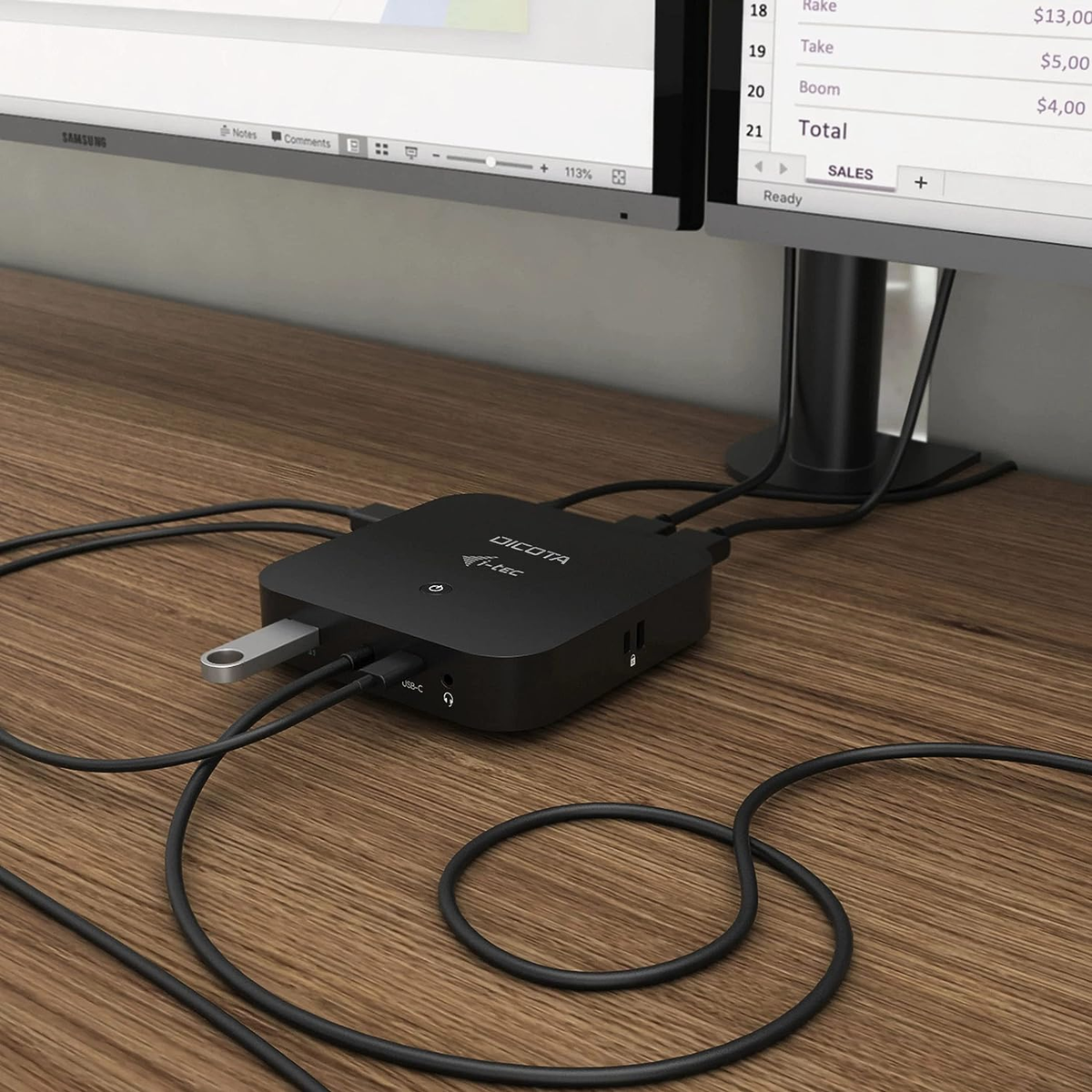 Schwarzer Hub mit USB-Laufwerk, angeschlossen an Monitore auf Holzschreibtisch.