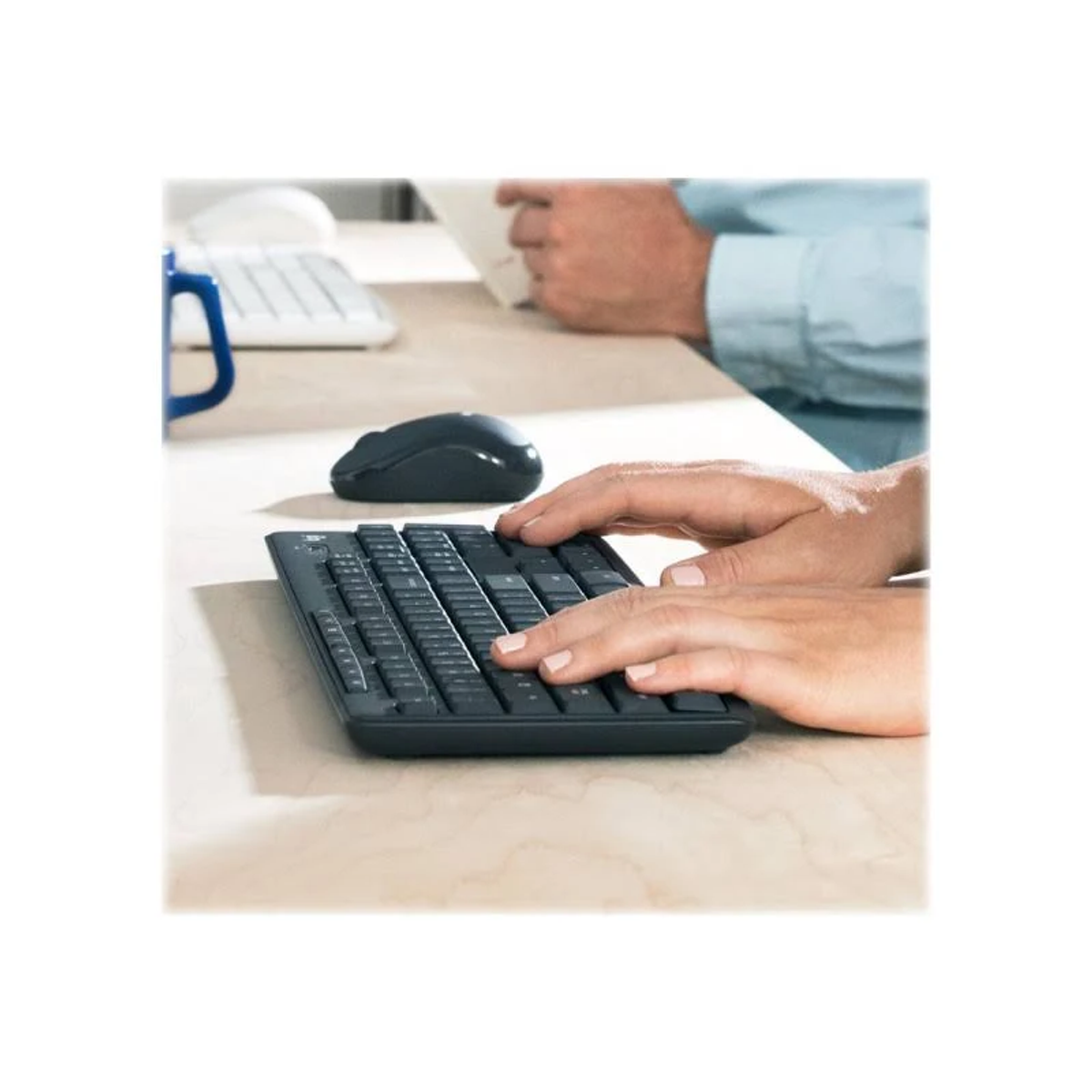 Hände tippen auf schwarzer Tastatur; Maus und andere Person am Schreibtisch.