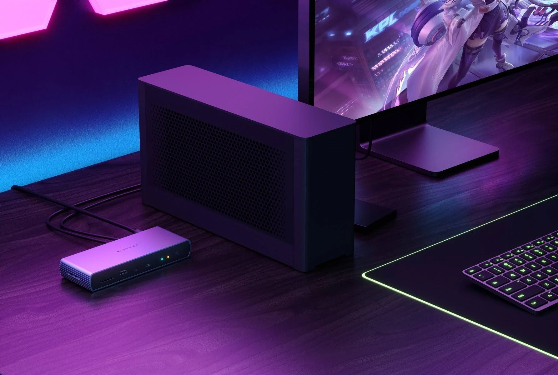Ein kleiner, dunkler Computer neben einer Dockingstation und einem Monitor. Lila und dunkler Hintergrund.