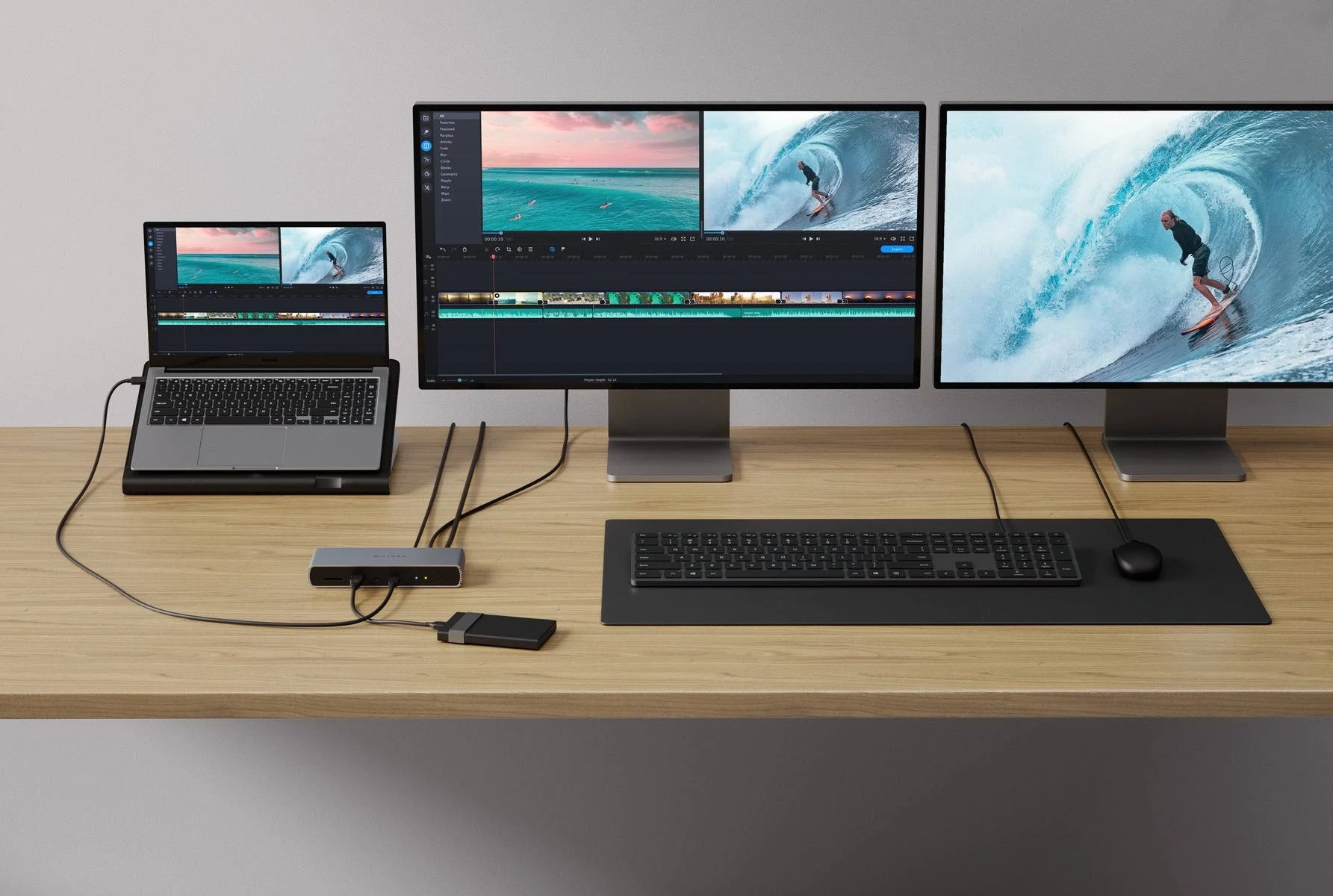 Arbeitsplatz mit Laptop, Monitor, Tastatur und Maus. Der Bildschirm zeigt Videoschnittsoftware. Der Hintergrund ist aus Holz.