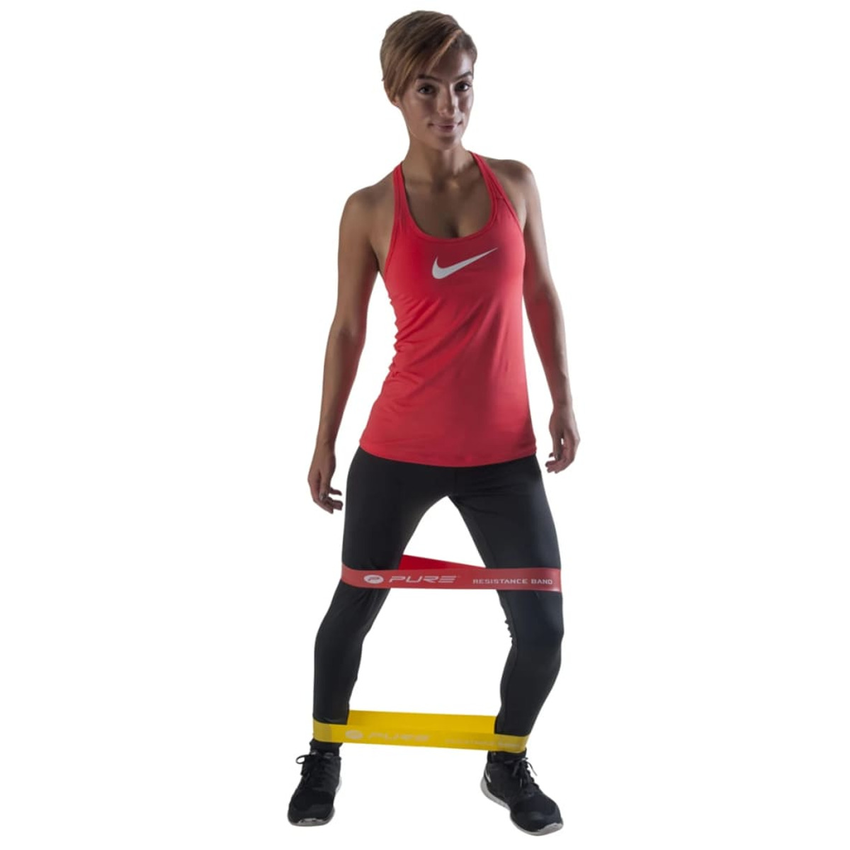 Eine Frau in Sportkleidung benutzt ein Widerstandsband. Rotes Oberteil, schwarze Hose und Schuhe, weißer Hintergrund.