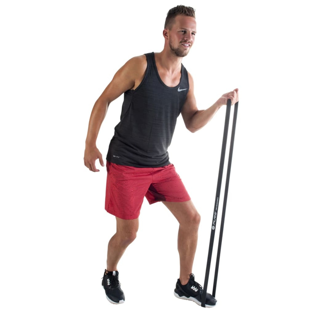 Mann trainiert mit Widerstandsbändern. Er trägt dunkles Tanktop und rote Shorts.