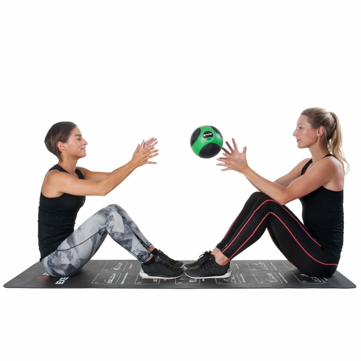 Zwei Frauen sitzen auf einer schwarzen Matte, eine wirft der anderen einen grünen Ball zu. Weißer Hintergrund.