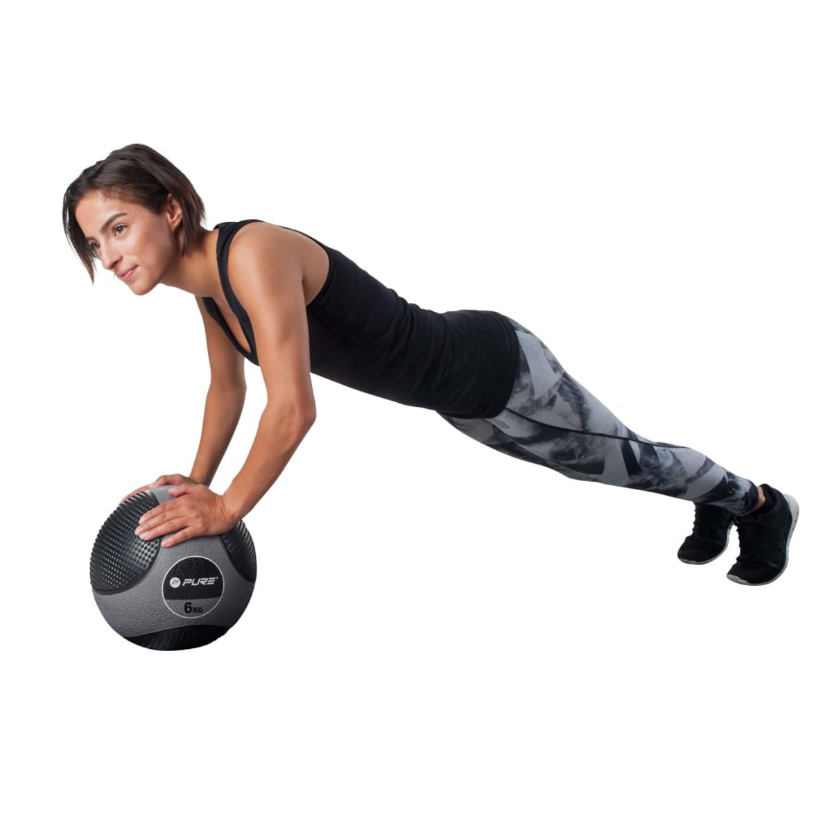 Donna che fa flessioni con una palla medica grigia. Indossa leggings e una canotta nera.