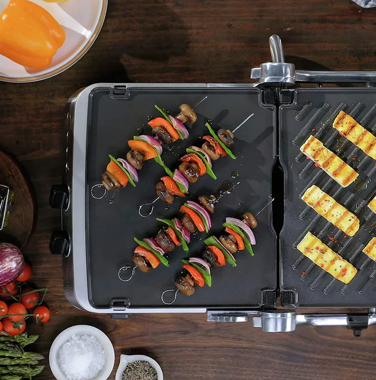 Widok z góry na grill z szaszłykami warzywnymi i serem halloumi. Warzywa to czerwona cebula, papryka i pieczarki.