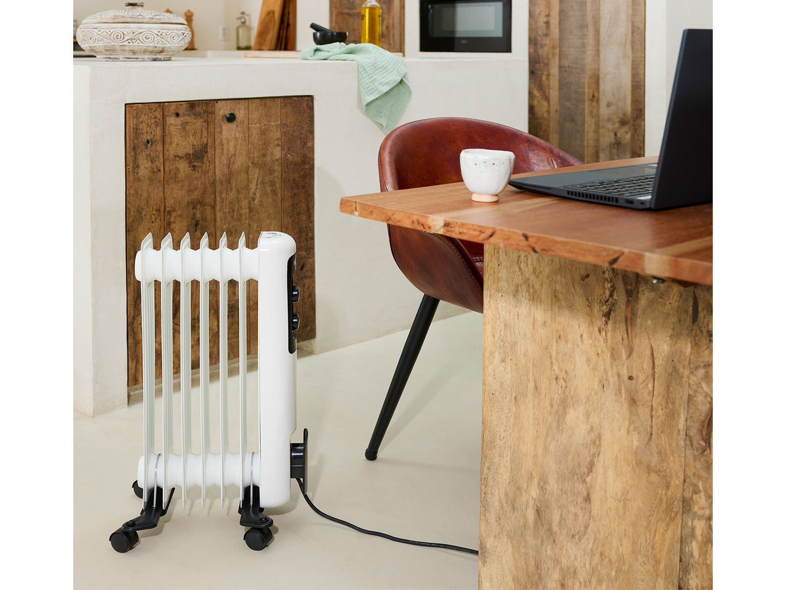 Ein weißer Heizkörper steht in der Nähe eines Holztisches mit Laptop und Stuhl in der Küche.