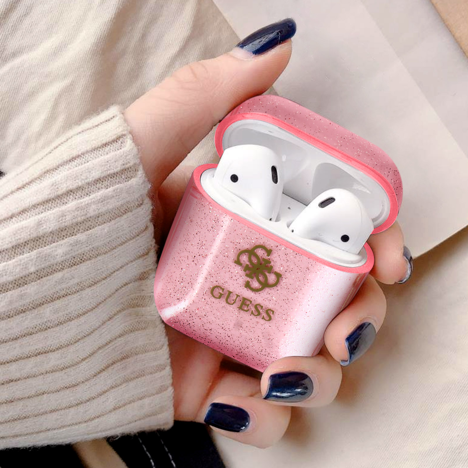 Una mano di donna che tiene una custodia Guess rosa con auricolari bianchi all'interno.