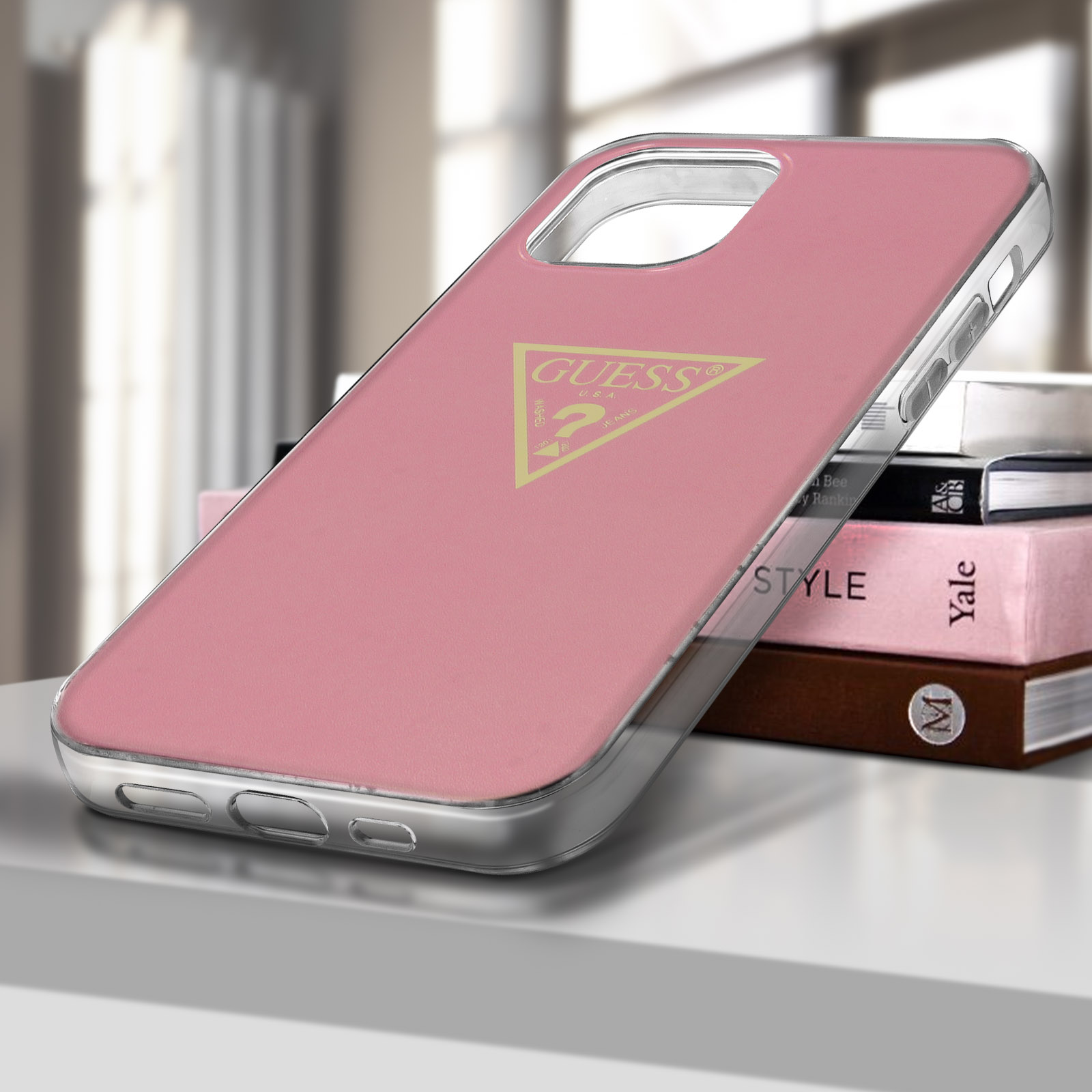 Custodia rosa per telefono con logo Guess, posizionata su libri e un tavolo.