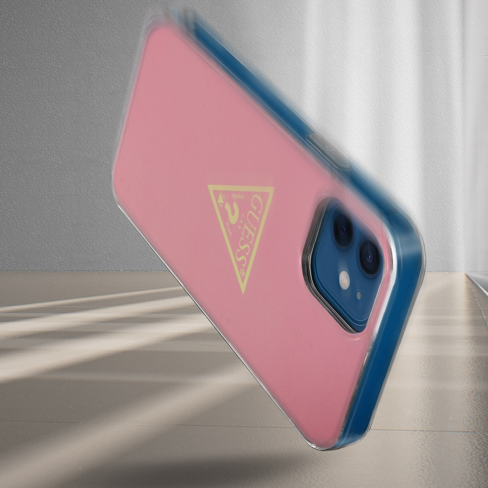 Custodia rosa per telefono con logo Guess, bordo blu, con sfondo sfocato.