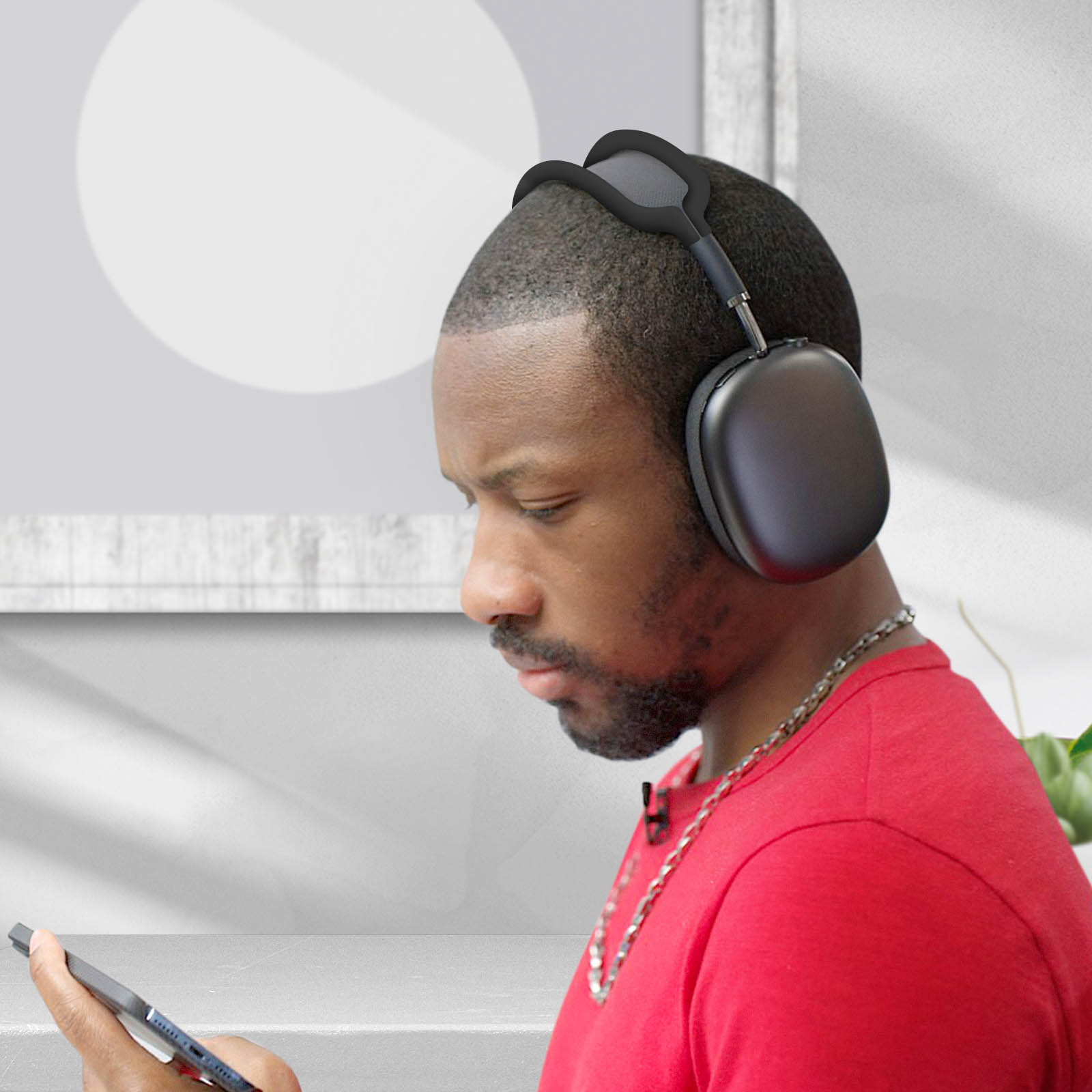 Hombre con auriculares negros mirando una tableta. Camisa roja. Pared blanca y fondo de planta.