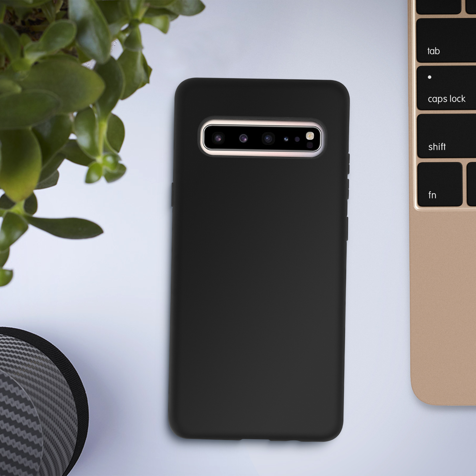 Custodia nera per telefono, telefono con più fotocamere, pianta e tastiera. Tavolo bianco.