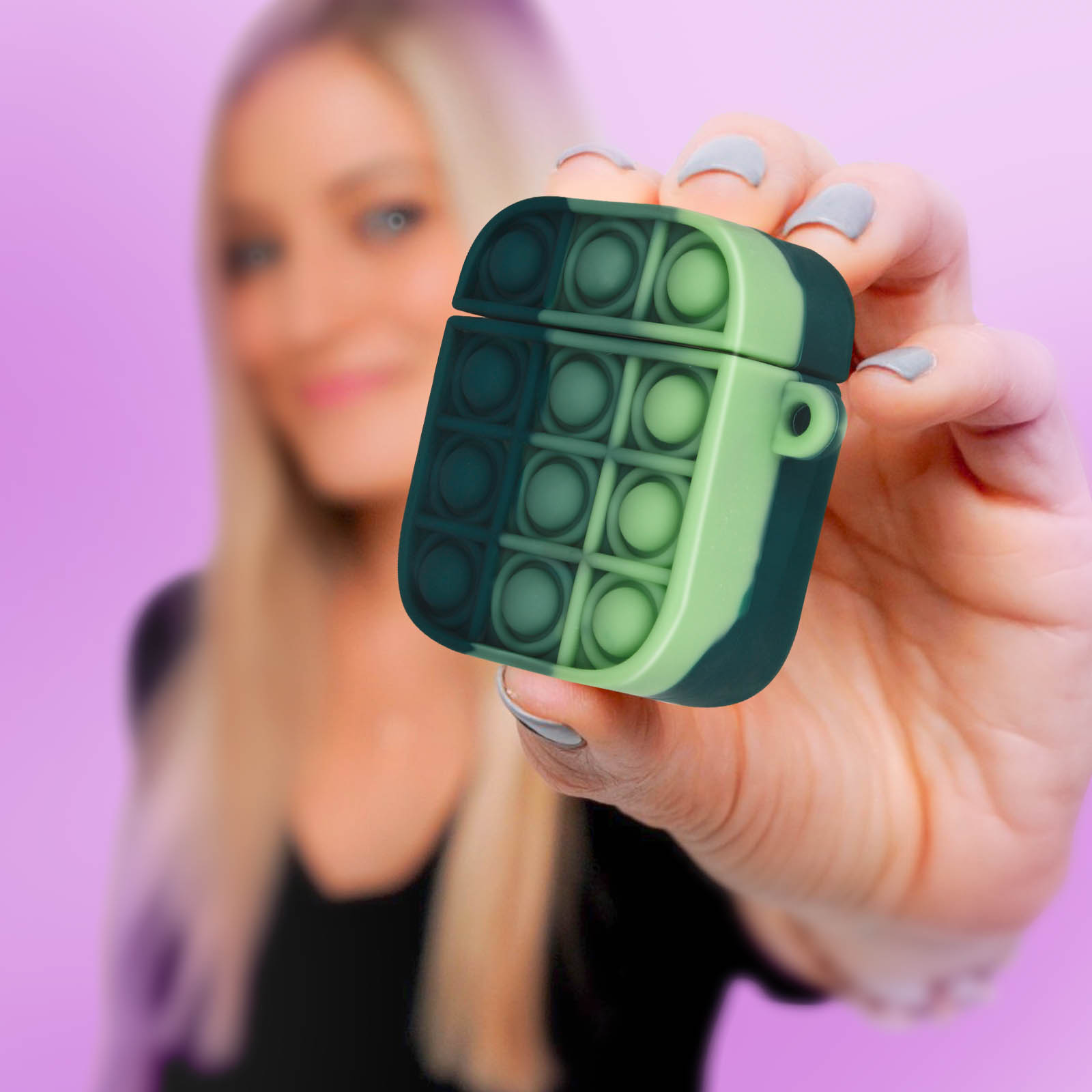 Persona sosteniendo una funda AirPods pop-it verde y azul contra fondo morado.