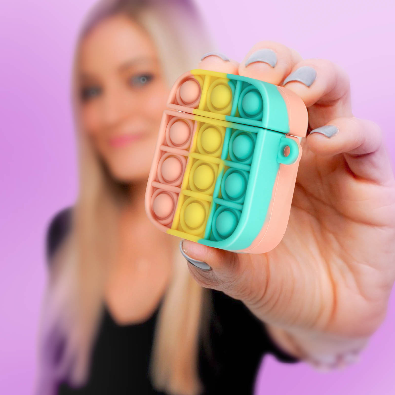 Persona sosteniendo una funda AirPod colorida estilo Pop-it. La funda es rosa, amarilla y turquesa.