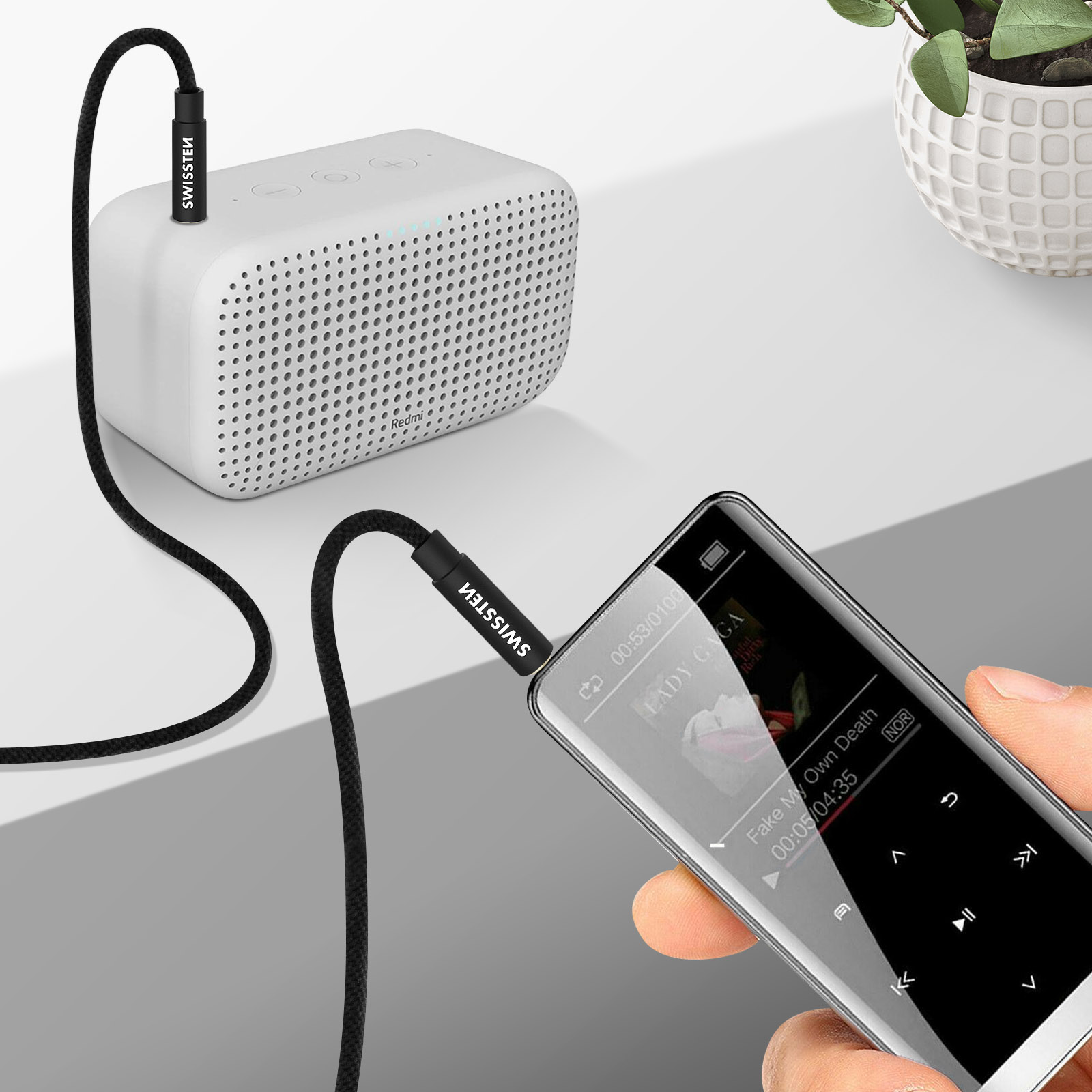 Ein weißer Lautsprecher und ein schwarzes Kabel, das mit einem Telefon verbunden ist, das Musik abspielt.