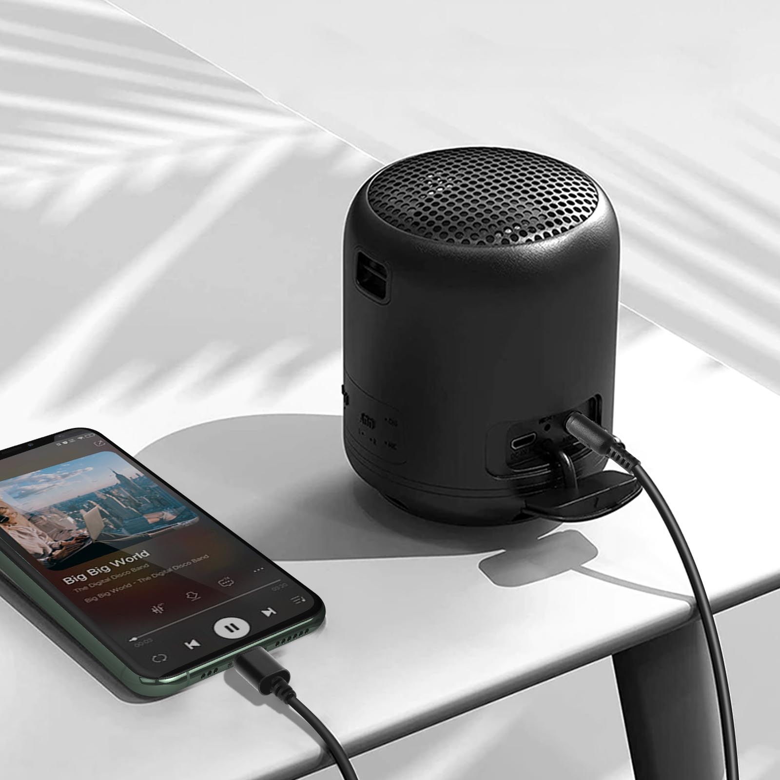 Altoparlante nero collegato a un telefono che mostra l'app musicale, su un tavolo bianco.
