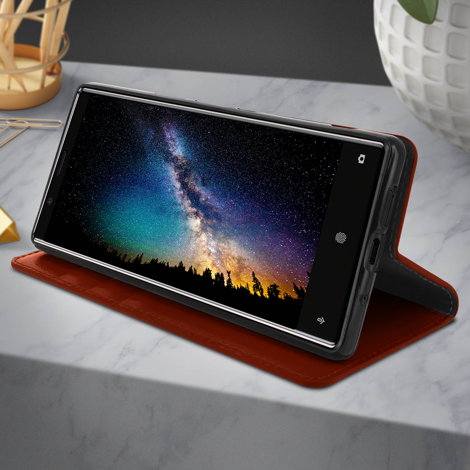 Smartphone in custodia di pelle marrone. Mostra un cielo notturno. Posizionato su una superficie di marmo.