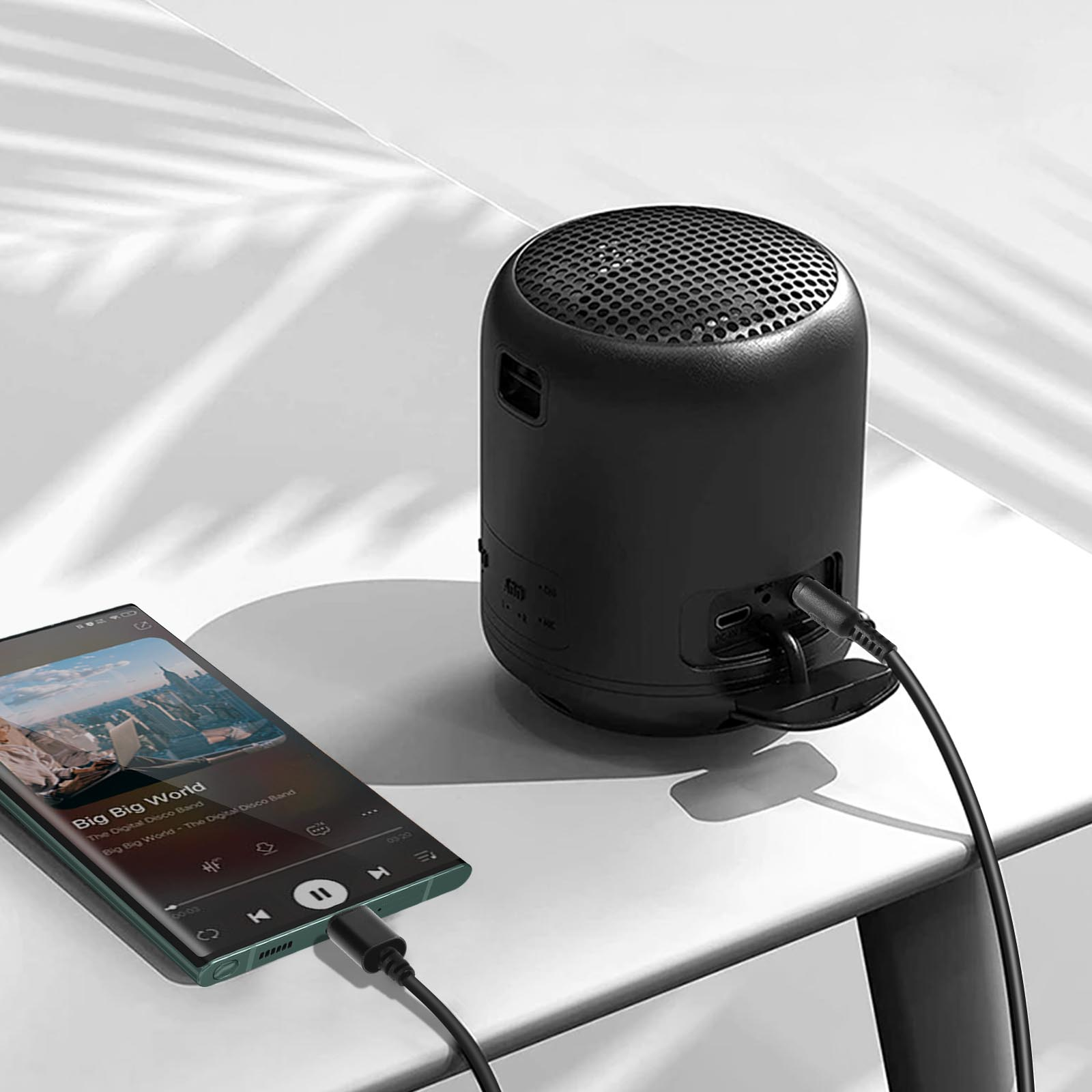 Un altavoz negro está conectado a un teléfono que reproduce música. El altavoz está sobre una superficie blanca.