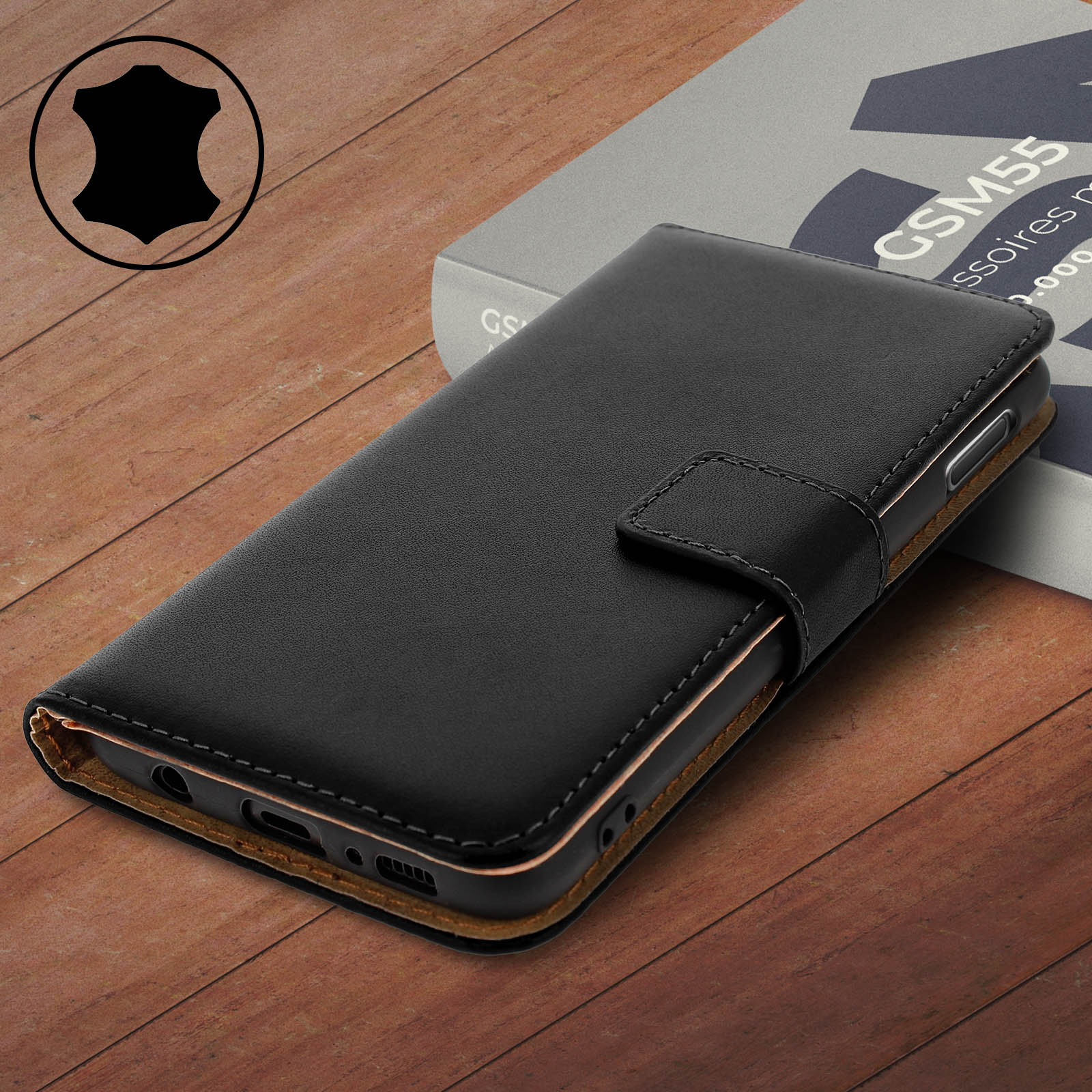 Custodia per telefono in pelle nera con patta, su una superficie di legno, con un libro sullo sfondo.