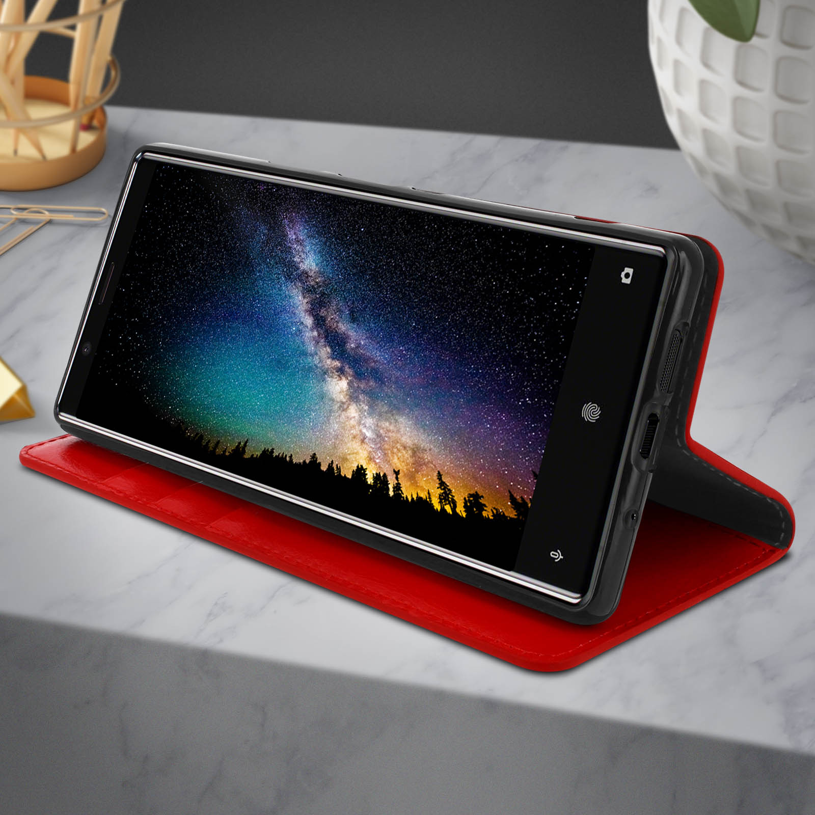 Uno smartphone in una custodia di pelle rossa, esposto su una superficie di marmo con un'immagine di notte stellata.