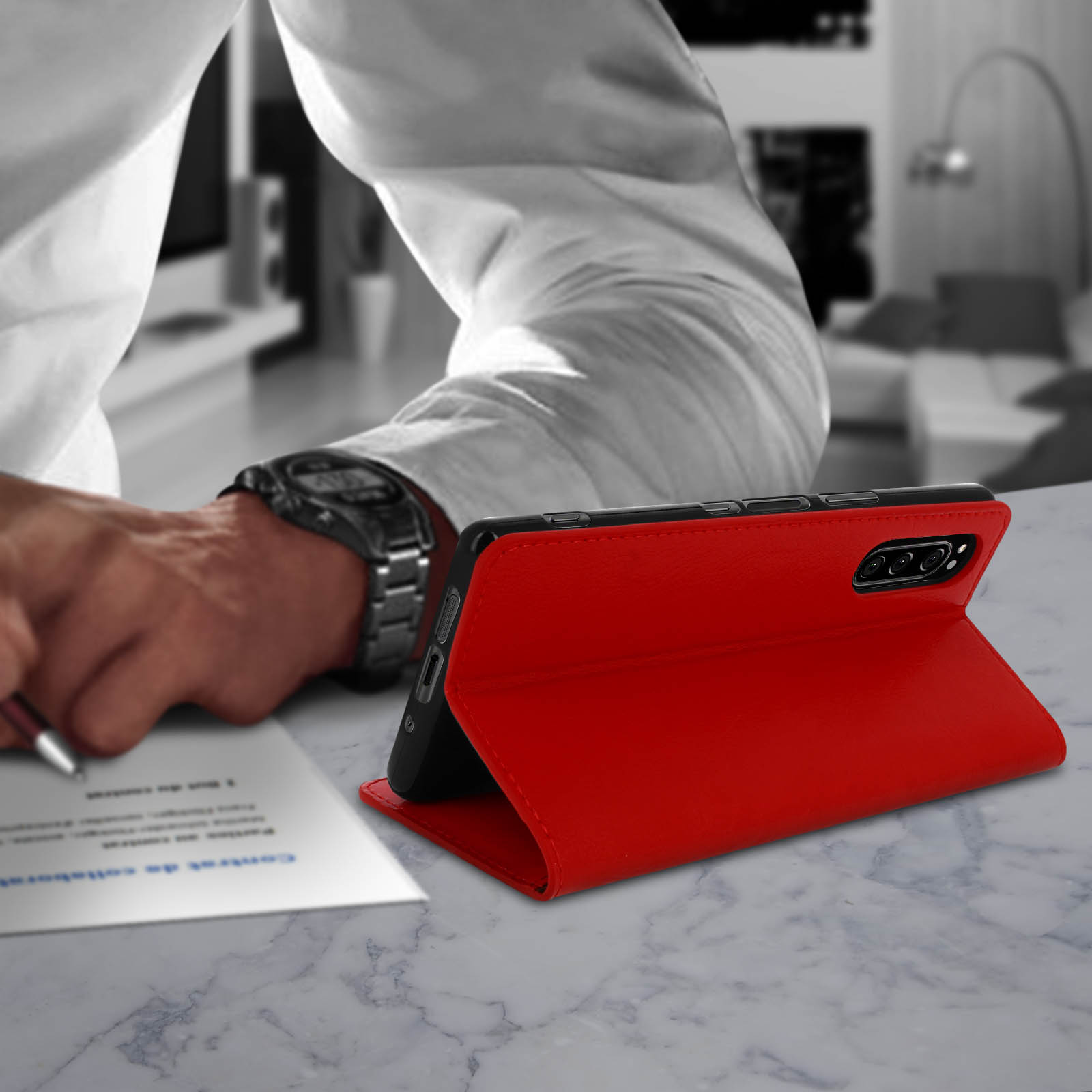 Custodia rossa per telefono, piegata, su superficie in marmo, persona che scrive.