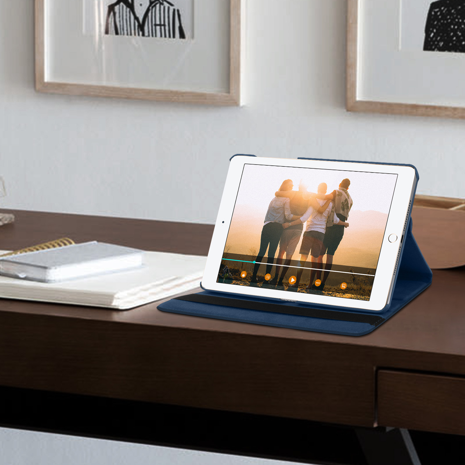Tablet che mostra un video. È in una custodia blu. Due foto incorniciate dietro.