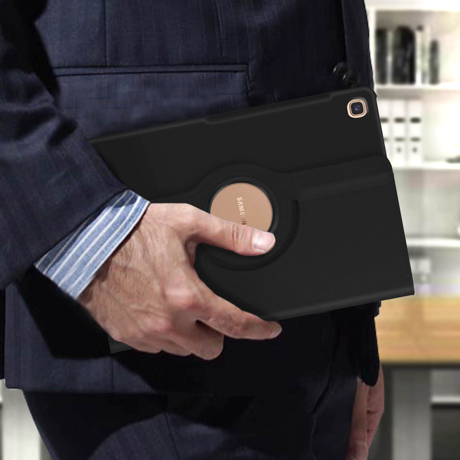 Persona in giacca e cravatta tiene custodia tablet nera con cerchio dorato, sfondo sfocato.
