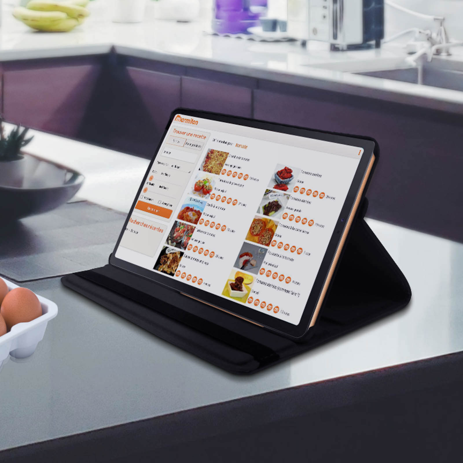 Tablet su custodia nera su piano cucina. Varie immagini di cibo. Sfondo grigio.