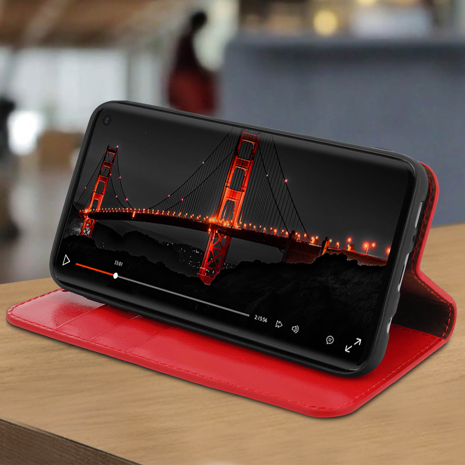 Smartphone in custodia rossa, che mostra un video di un ponte di notte.