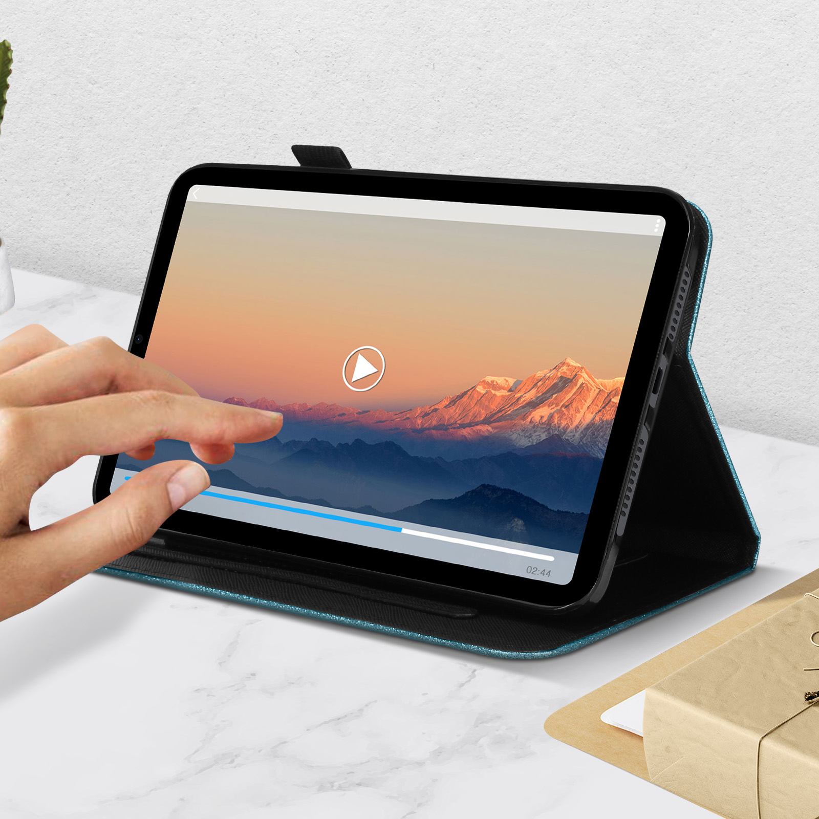 Mano che tocca lo schermo di un tablet con video, con custodia blu su superficie di marmo.