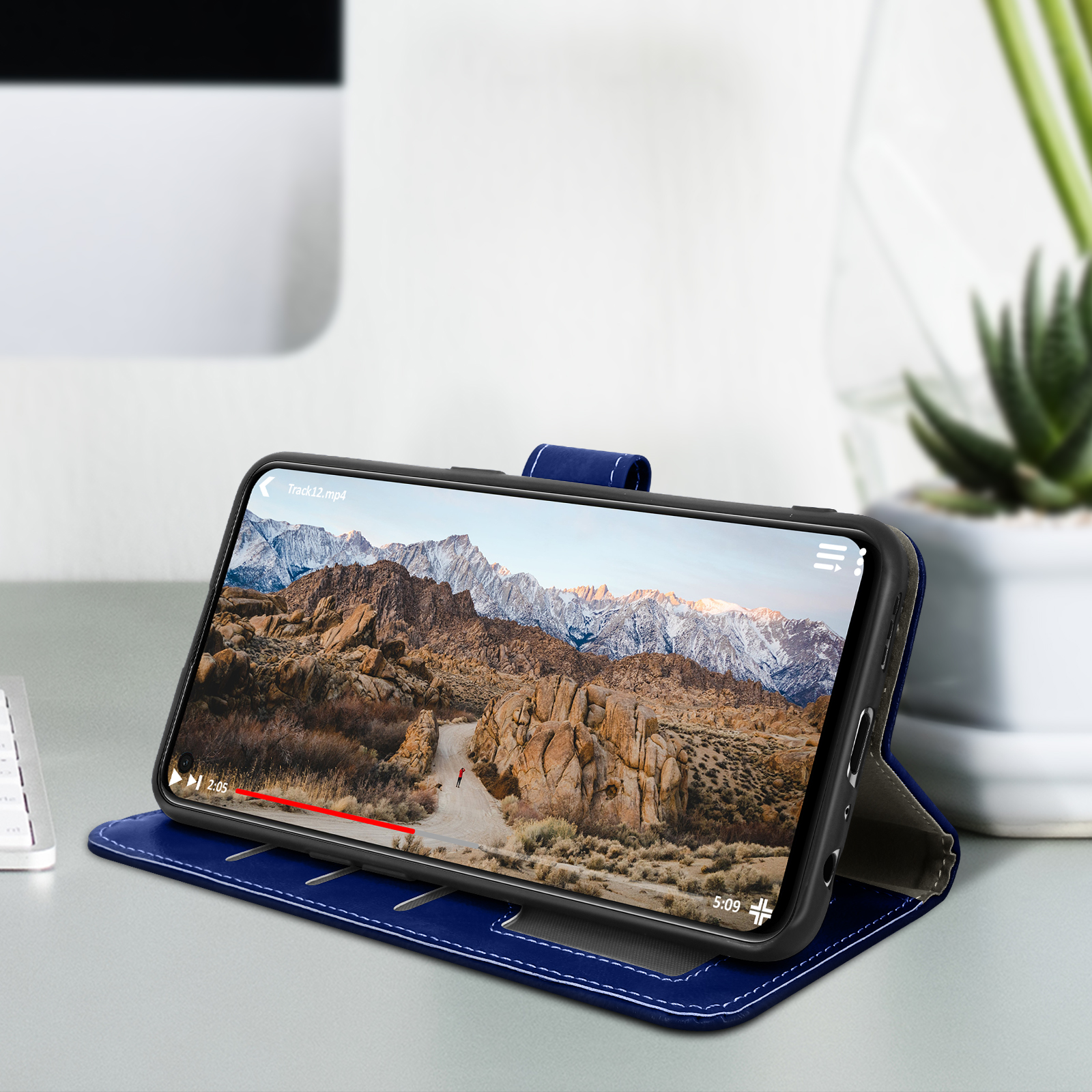 Smartphone dans un étui en cuir bleu, soutenu. Vidéo en cours de lecture. Bureau et plante visibles.