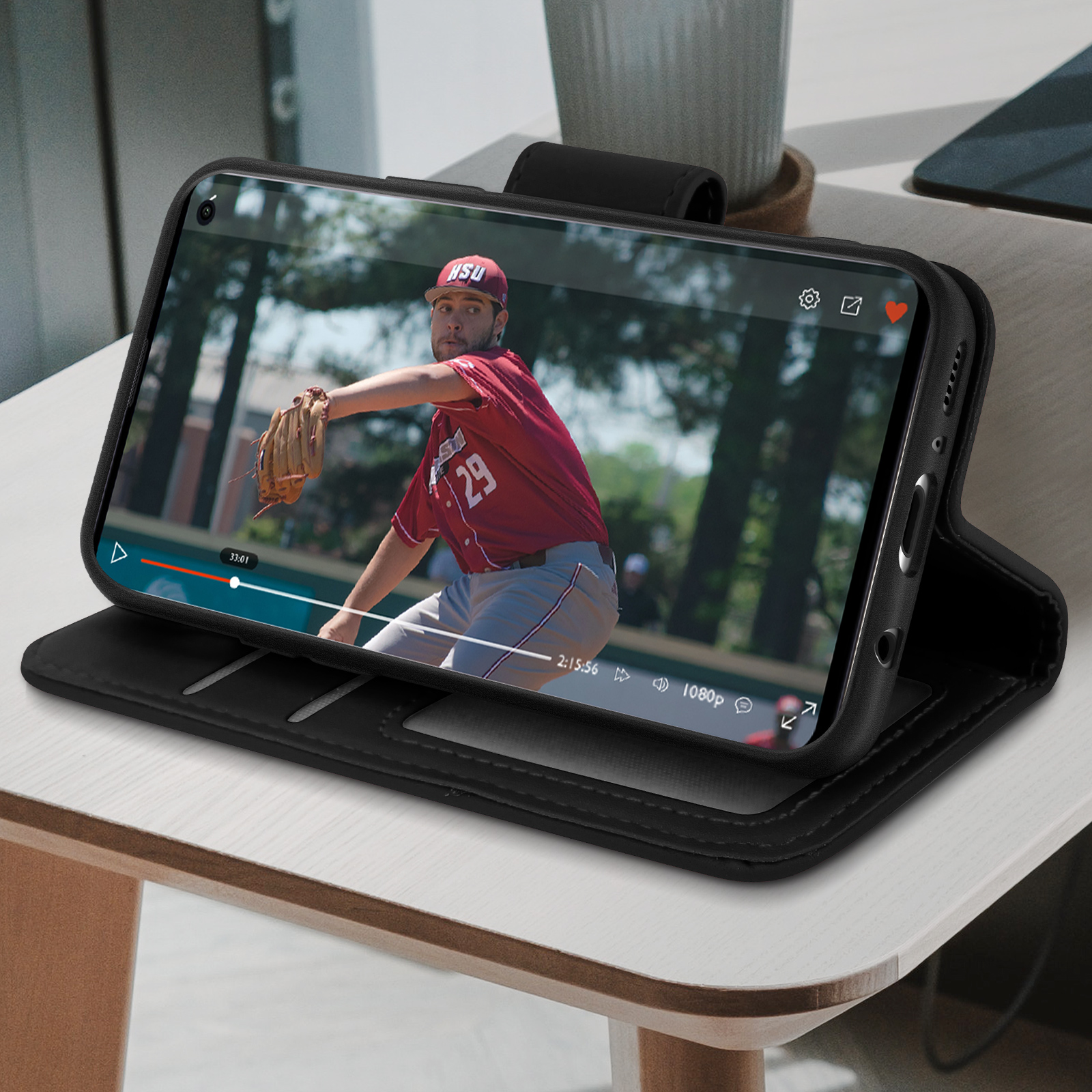 Een zwarte smartphone met een video die op het scherm wordt afgespeeld, in een zwarte case op een houten tafel.