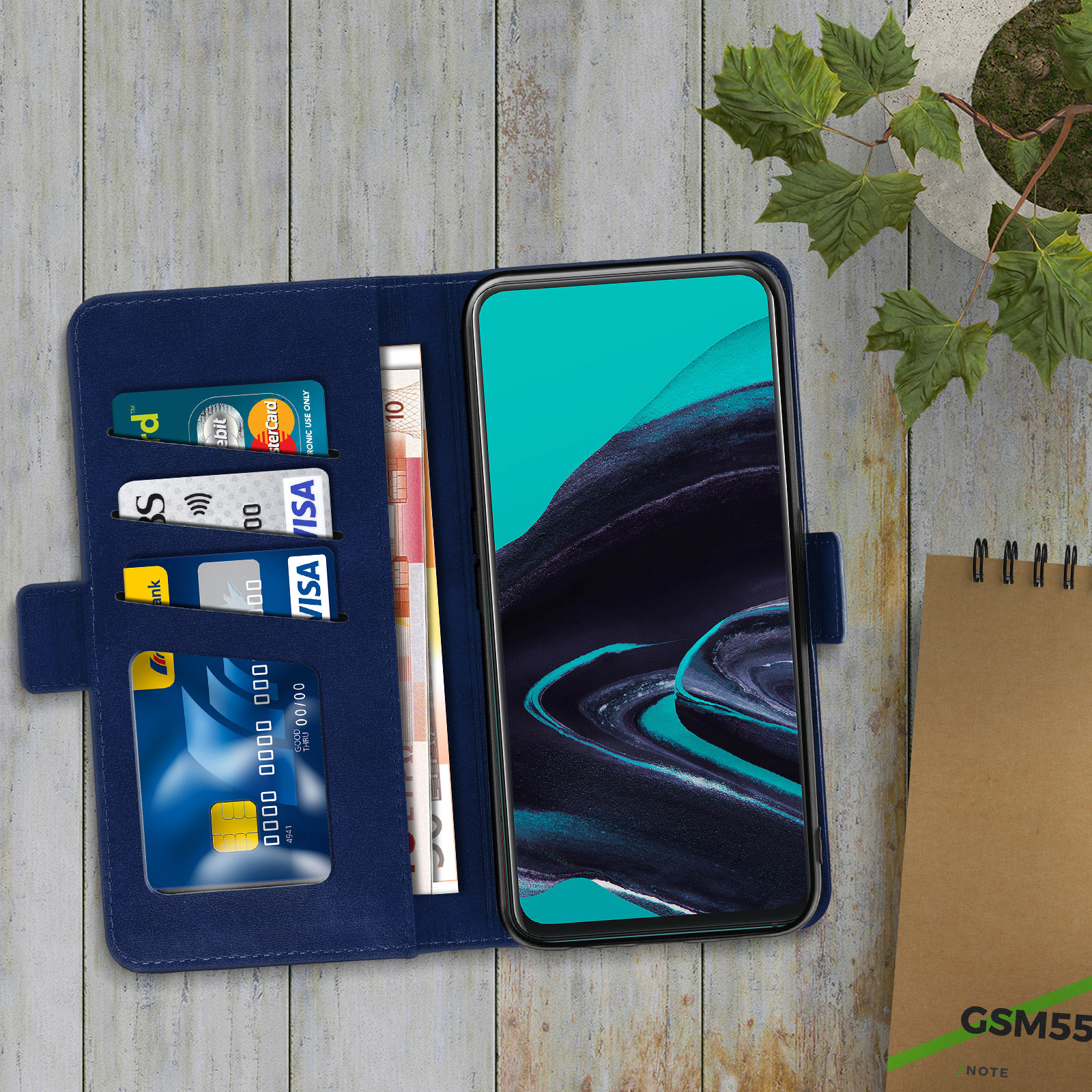 Étui de téléphone bleu ouvert avec cartes et argent liquide à l'intérieur, sur une table en bois. Plante et bloc-notes à proximité.