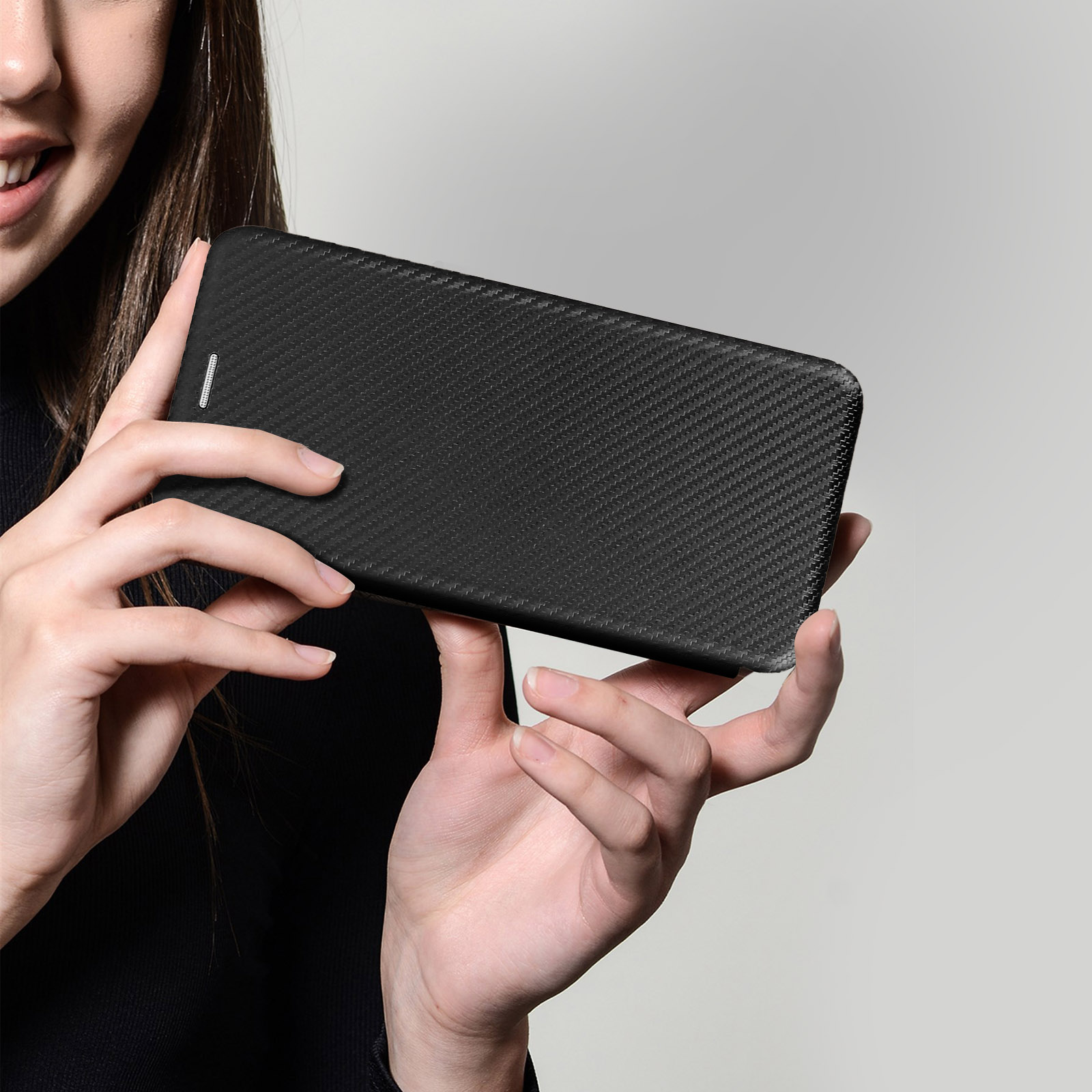 Una donna tiene in mano una custodia nera per telefono con texture in fibra di carbonio.
