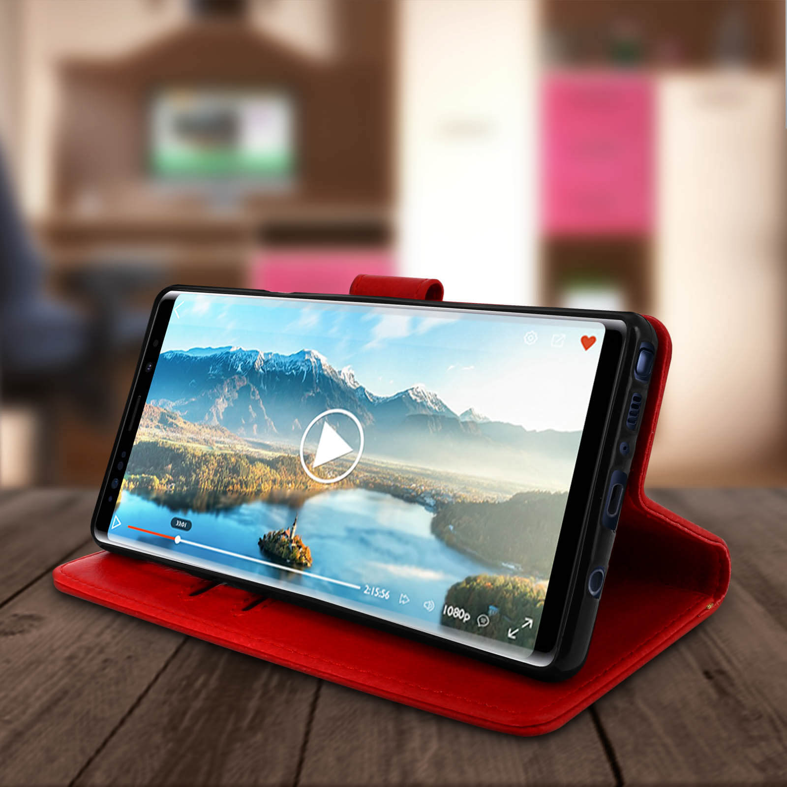 Smartphone con video su custodia rossa, appoggiato su tavolo legno.