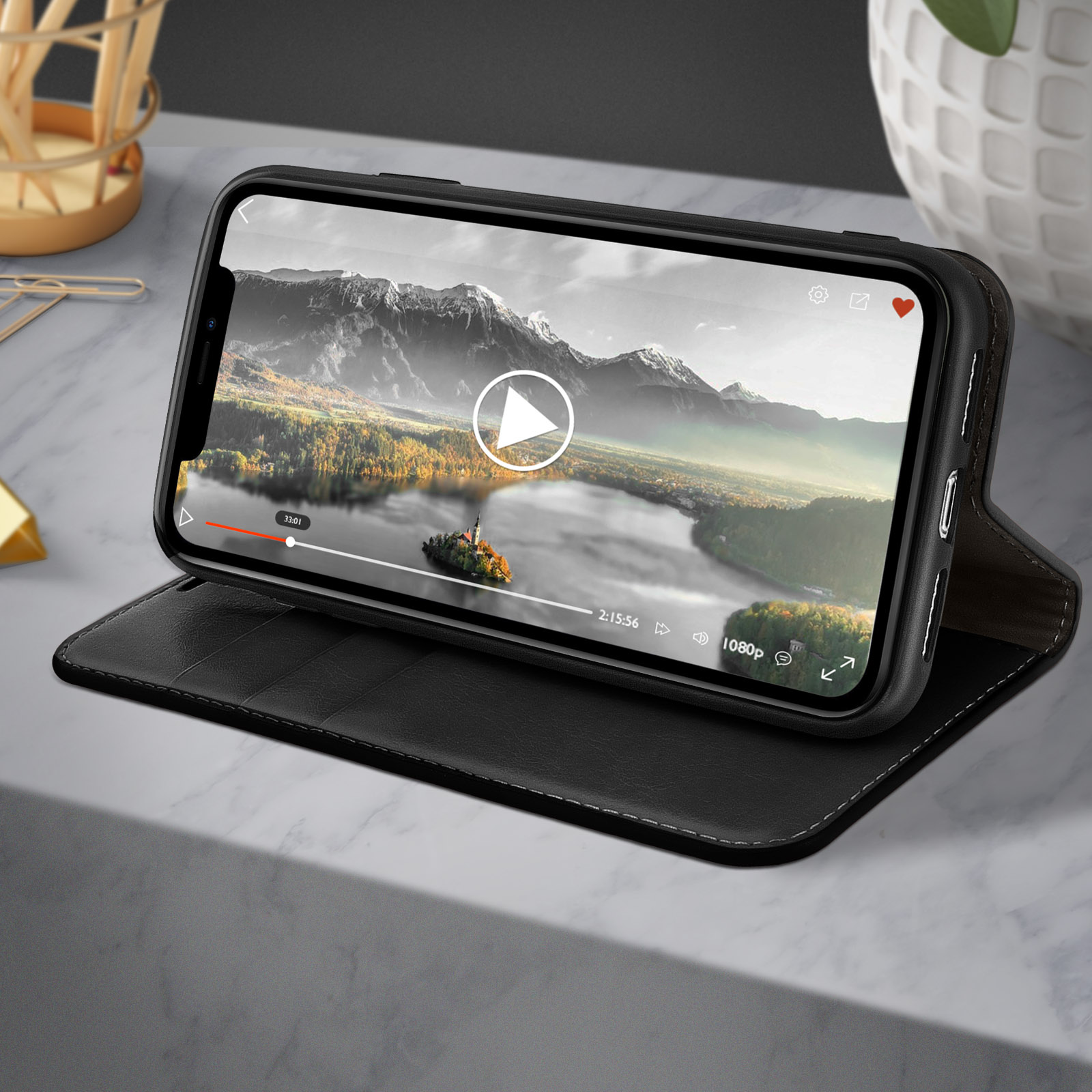 Een telefoon in een zwarte hoes staat op een marmeren oppervlak. Het scherm speelt een video af.