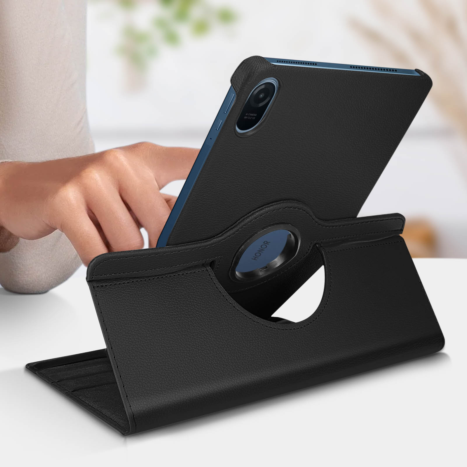 Tablet su supporto, custodia in pelle nera, con anello argentato e mano di una persona.