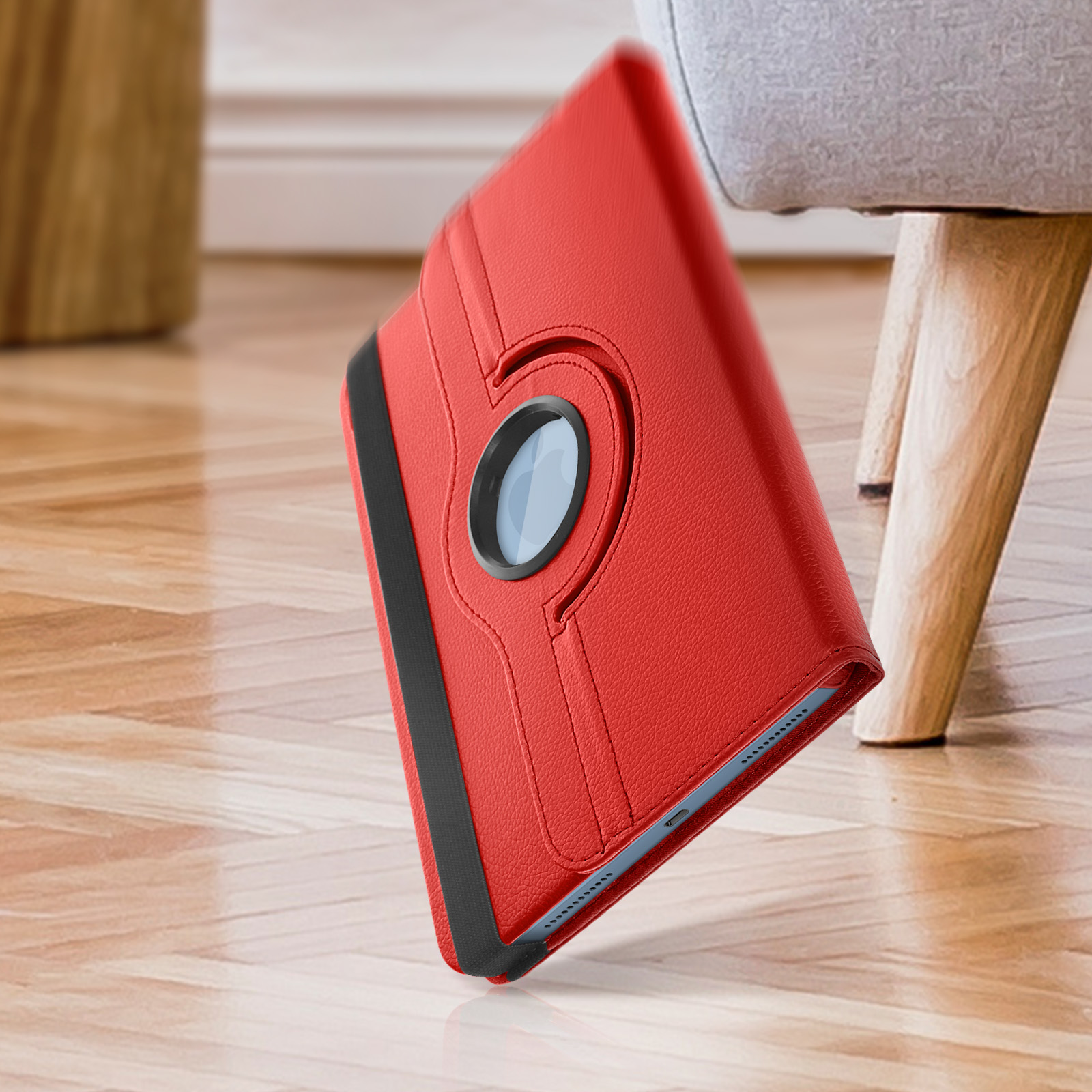 Eine rote Tablethülle mit Drehring ist abgewinkelt, mit Holzboden und einem Stuhlbein im Hintergrund.