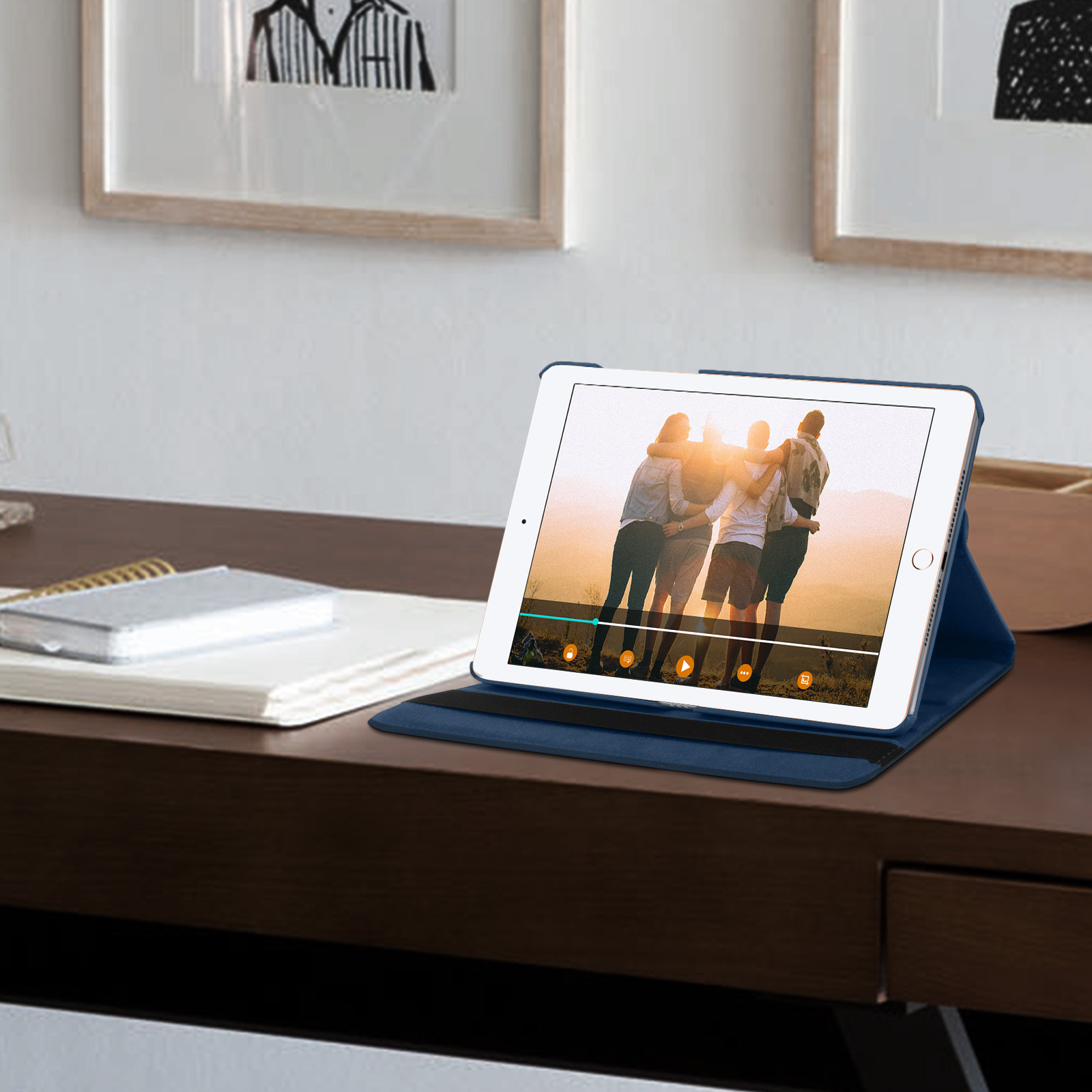 Tablet in custodia blu su scrivania in legno scuro che riproduce video. Persone sullo schermo. Muro bianco e arte sullo sfondo.