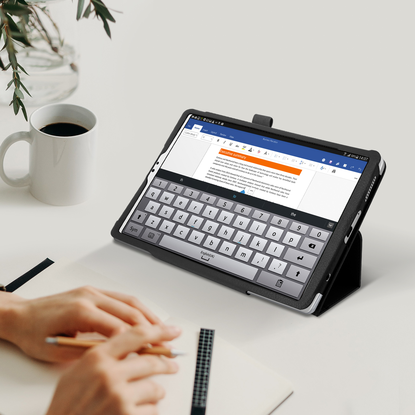 Tablet con custodia per tastiera su un tavolo bianco. Mano che tiene una penna. Testo sullo schermo.
