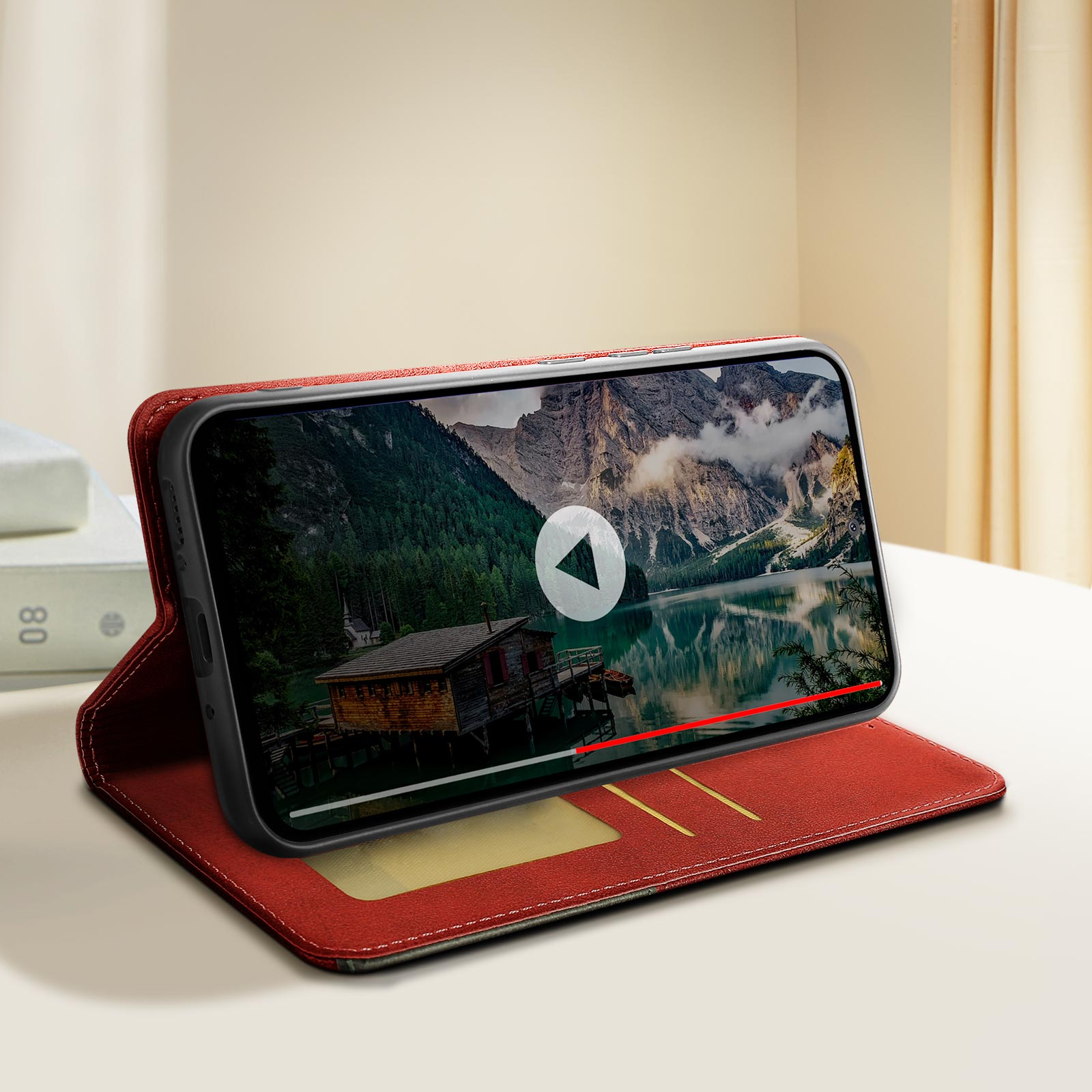 Telefono in custodia rossa, riproduce video con lago e montagne, aperto su tavolo.