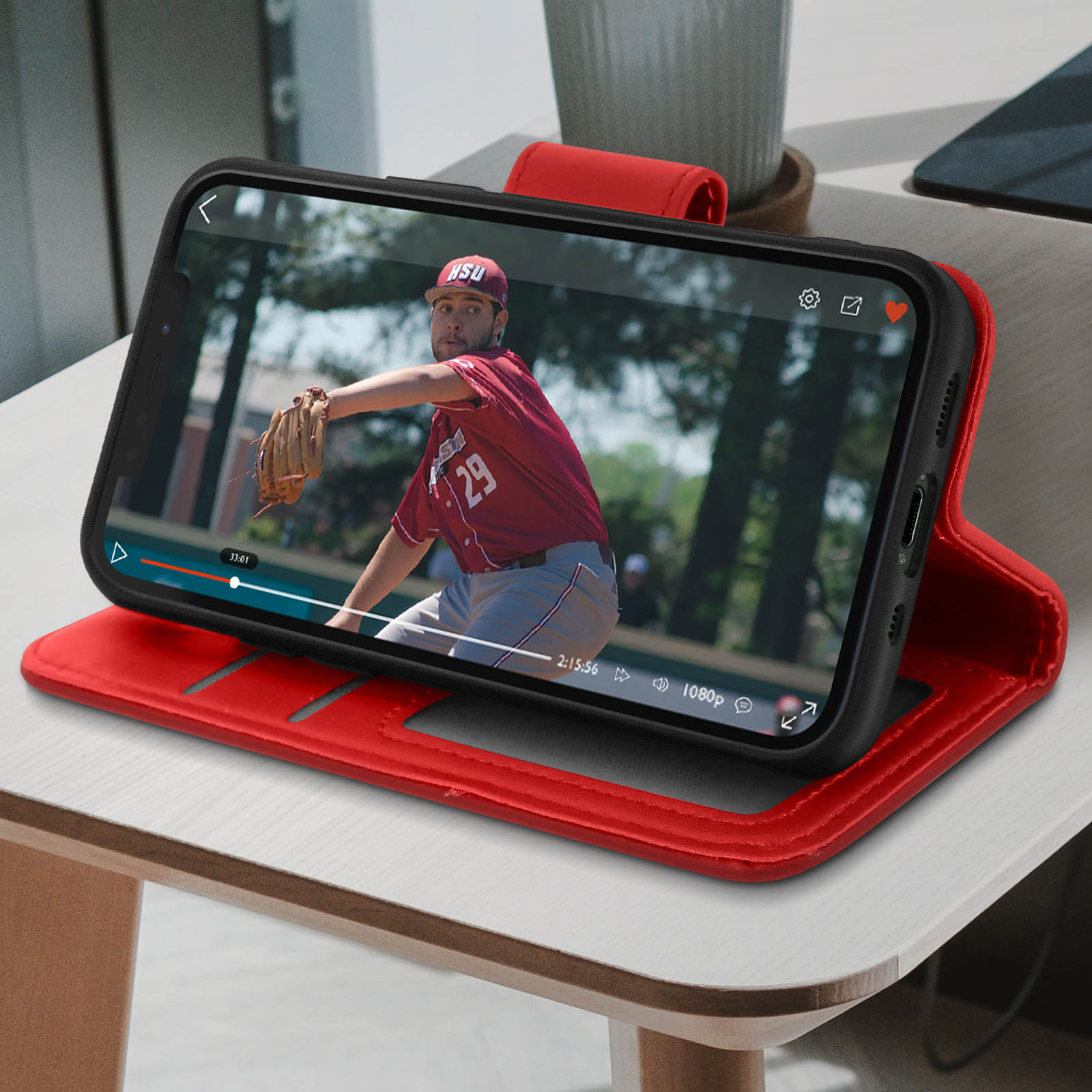 Telefono in custodia rossa mostra partita di baseball. Un giocatore lancia la palla. Custodia rossa su tavolo marrone.