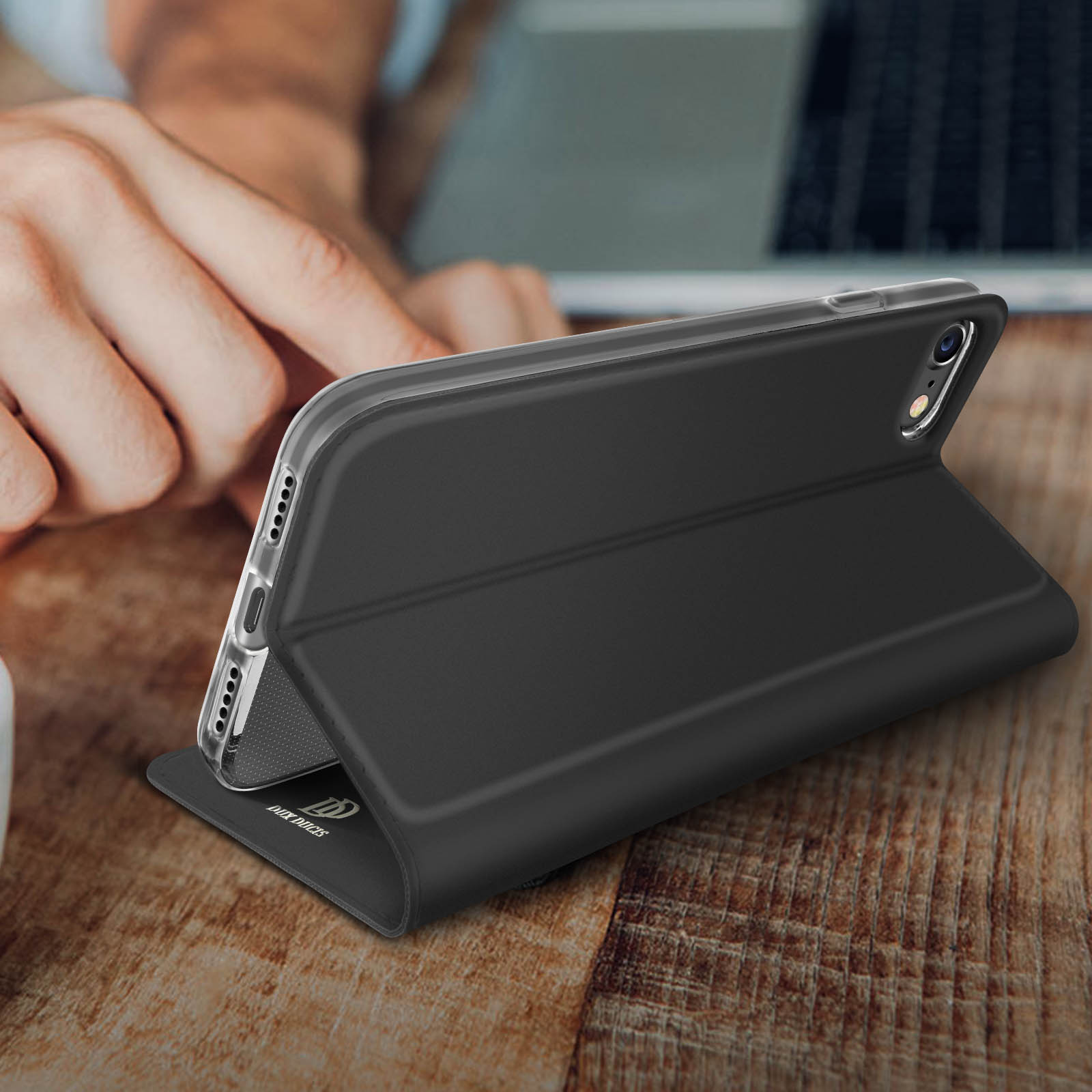 Zwarte telefoon in zwarte hoes, op houten tafel met hand op de achtergrond.