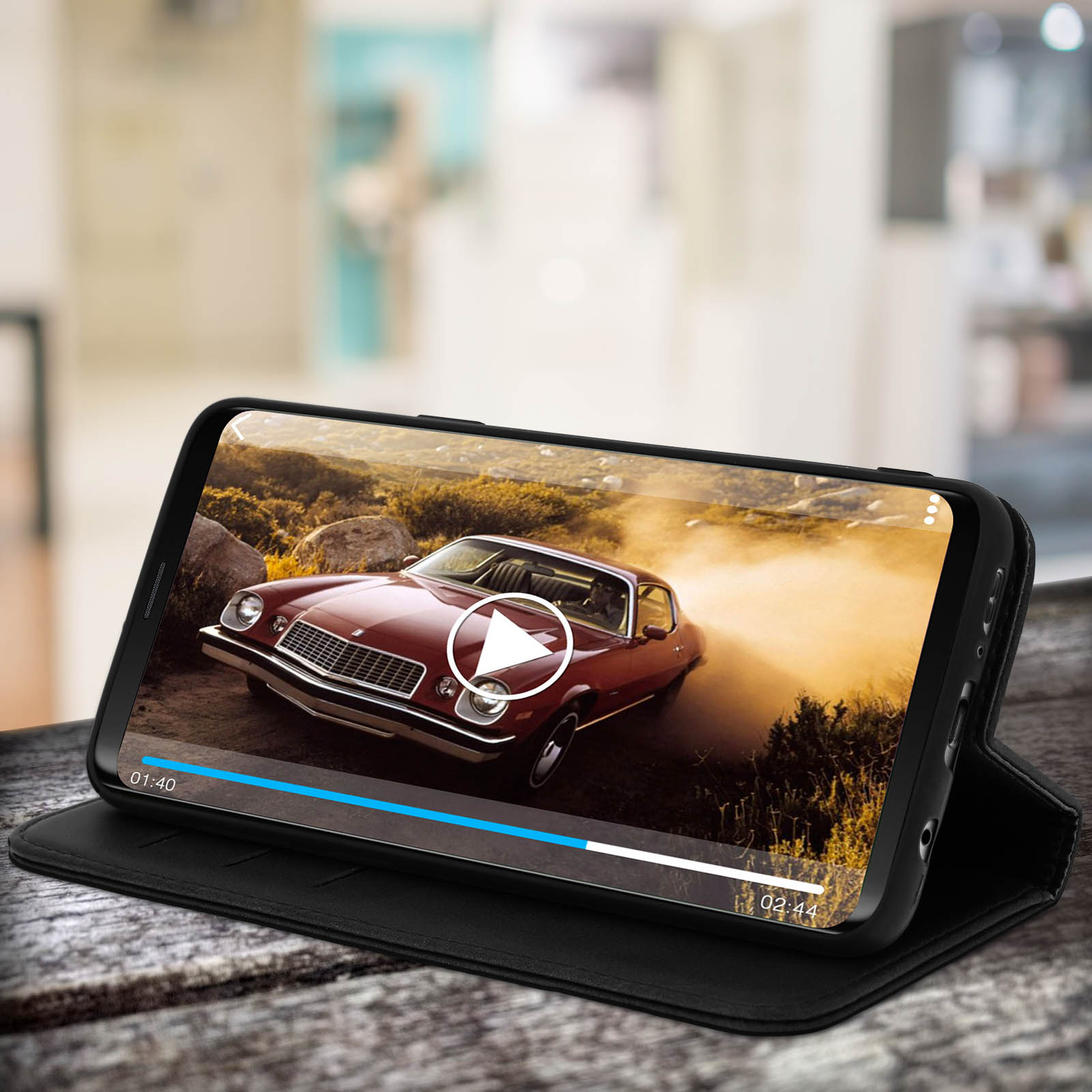 Telefono che mostra video di auto. Custodia nera su superficie in legno.