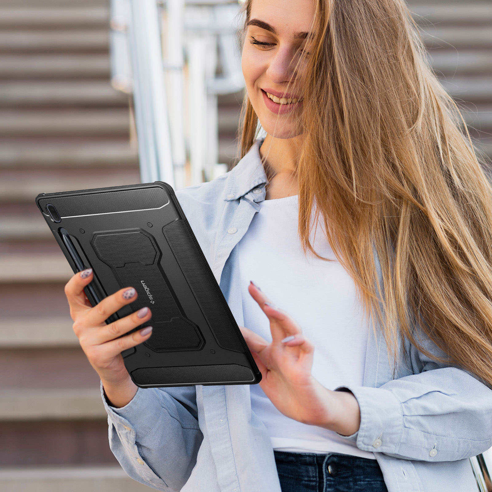 Donna che tiene un tablet con custodia e stilo neri, sorridente davanti alle scale.