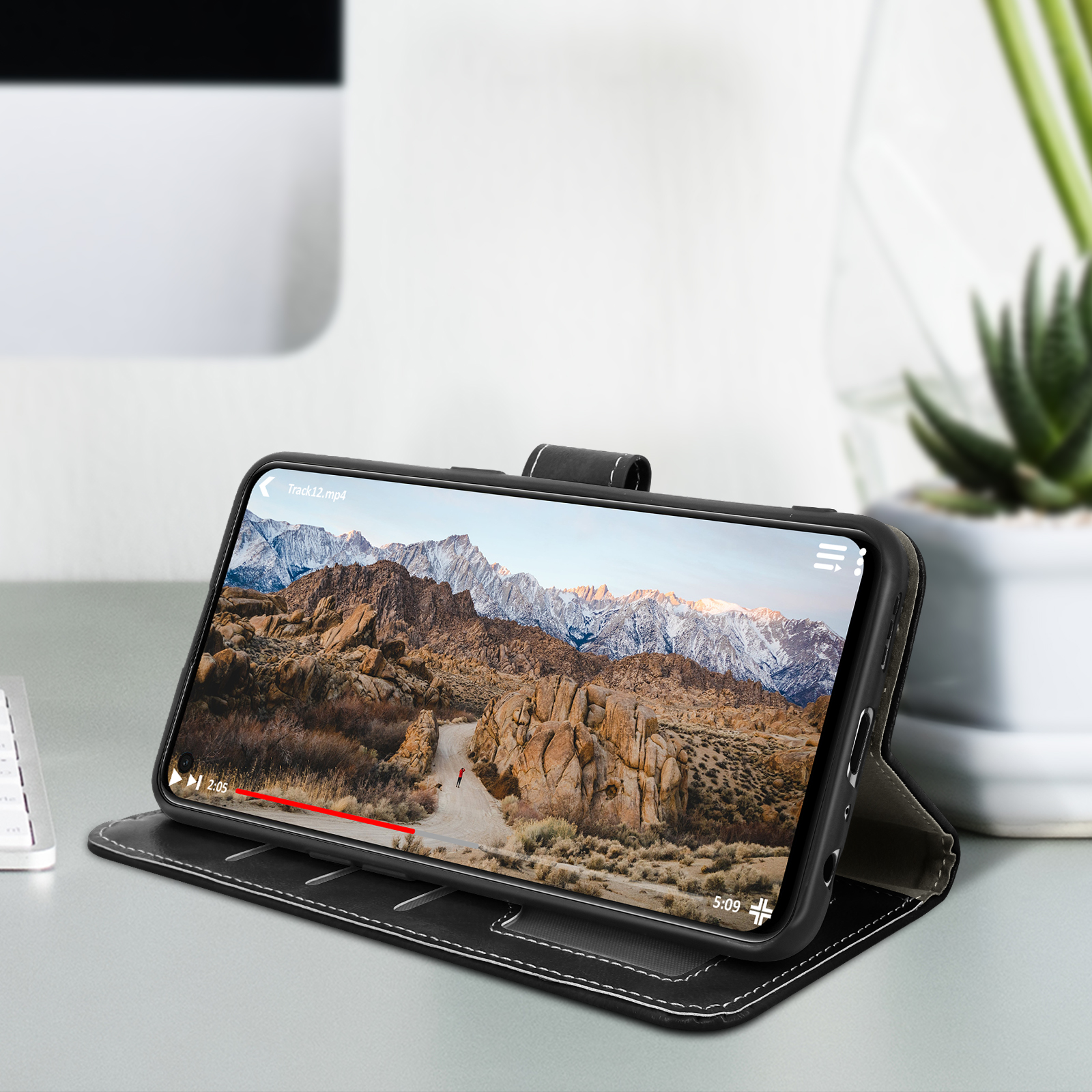 Un téléphone affichant une vidéo sur un étui noir sur une table. Un clavier blanc en arrière-plan.