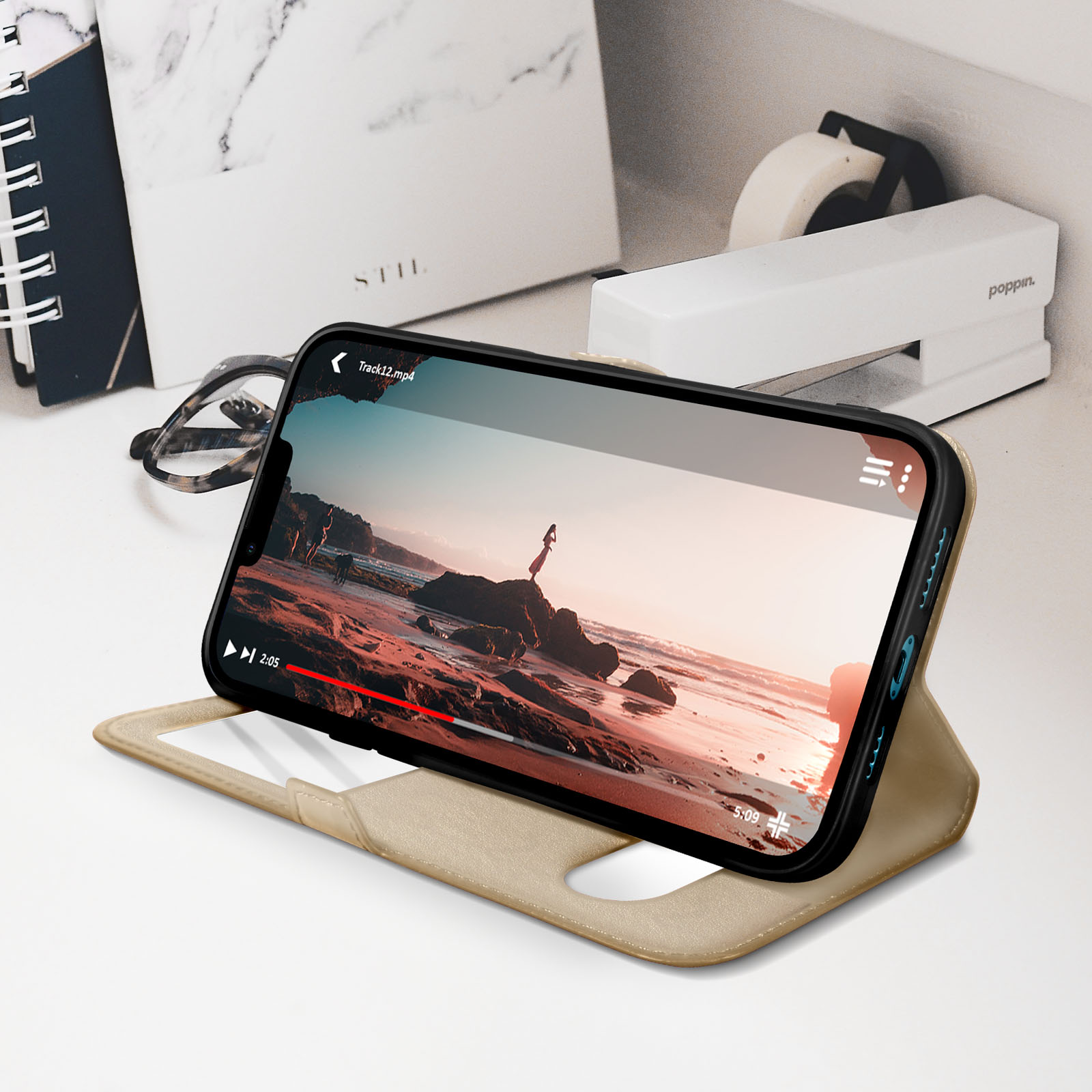 Smartphone con custodia beige che mostra un video. Il telefono è appoggiato. Lo sfondo include cancelleria.