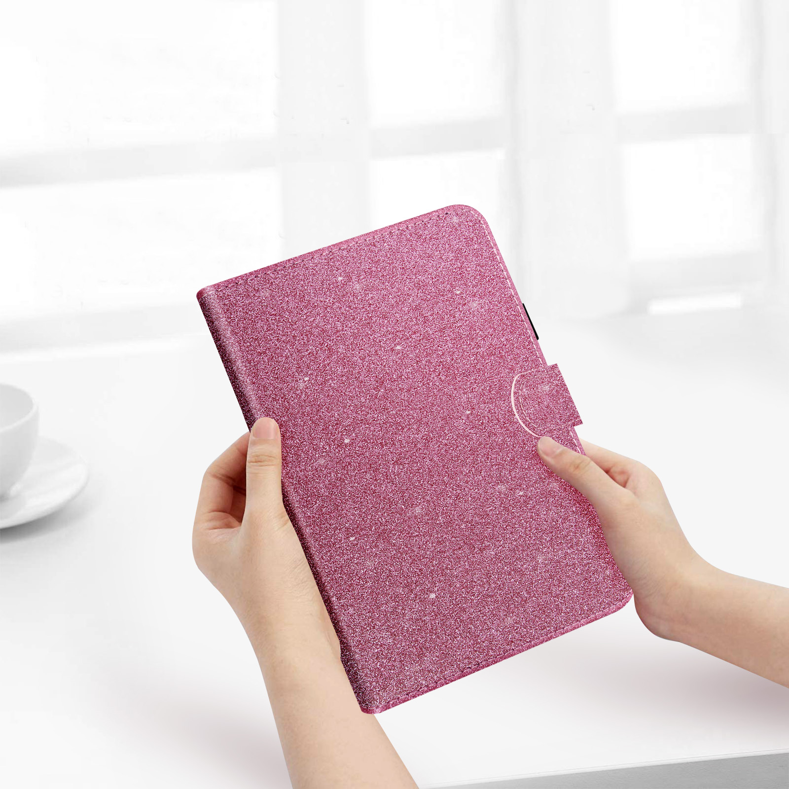 Mani che tengono una custodia per tablet rosa glitterata. Tavolo bianco. Sfondo Windows.