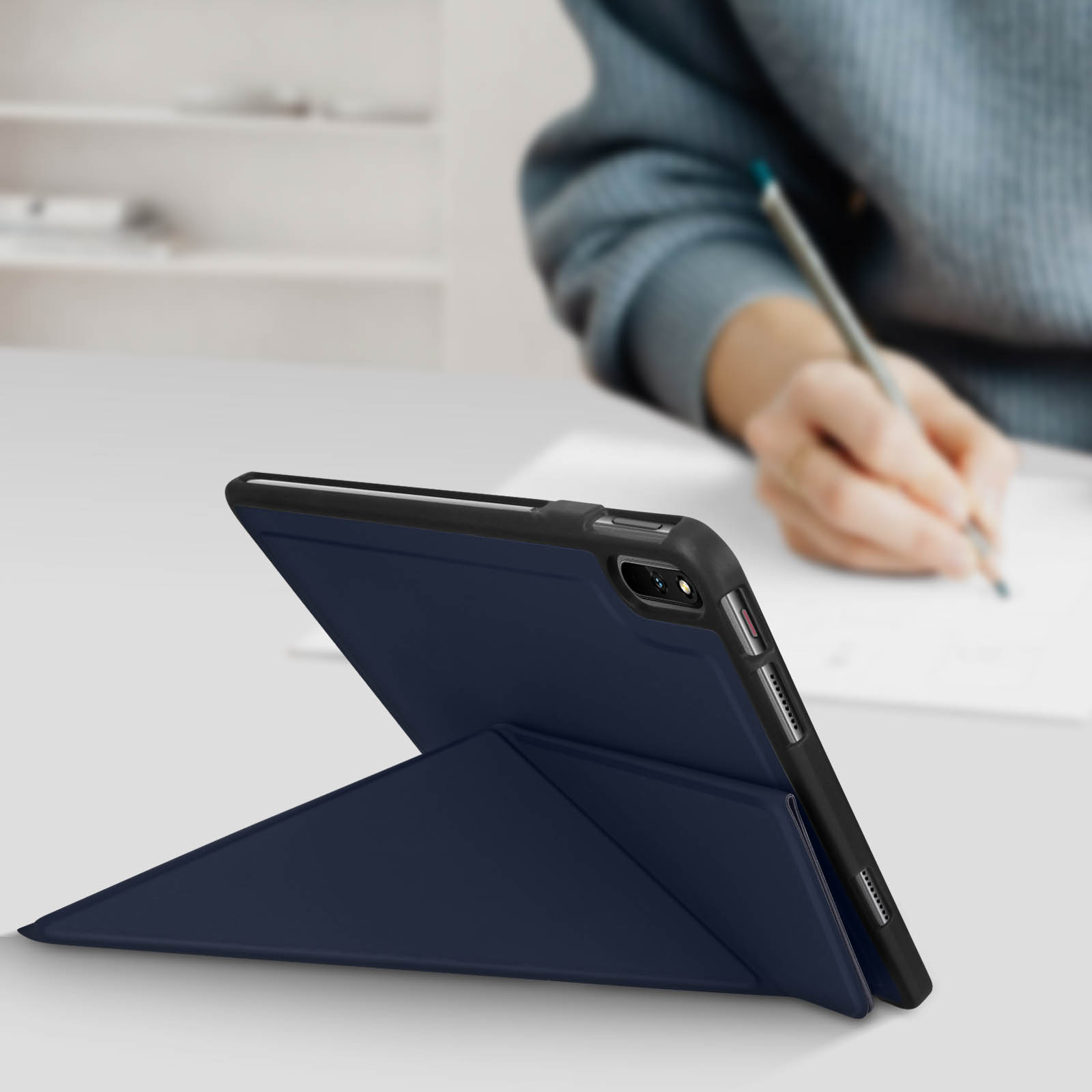 Custodia blu per tablet, aperta su un tavolo, persona che scrive sullo sfondo.