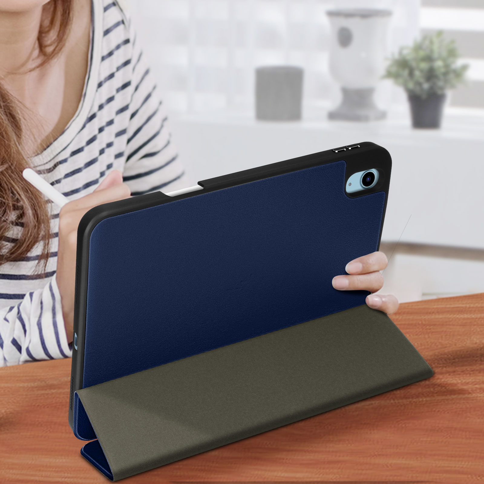 Un tablet in una custodia blu, aperto. Una mano lo tiene, con una penna visibile. Un tavolo di legno sullo sfondo.